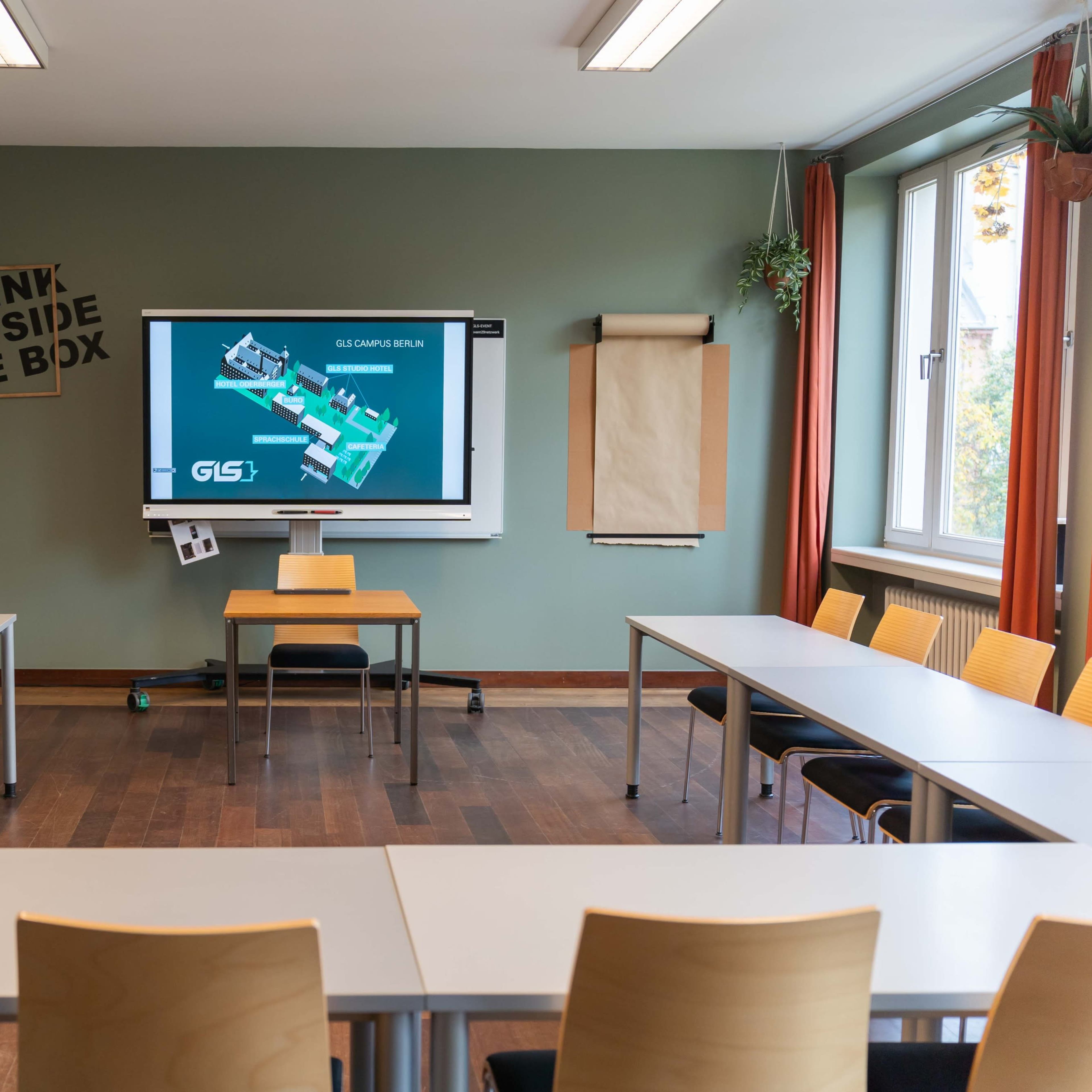 A classroom is arranged with tables in a U-shape, featuring a projector screen displaying a presentation, and walls adorned with minimal decorations.