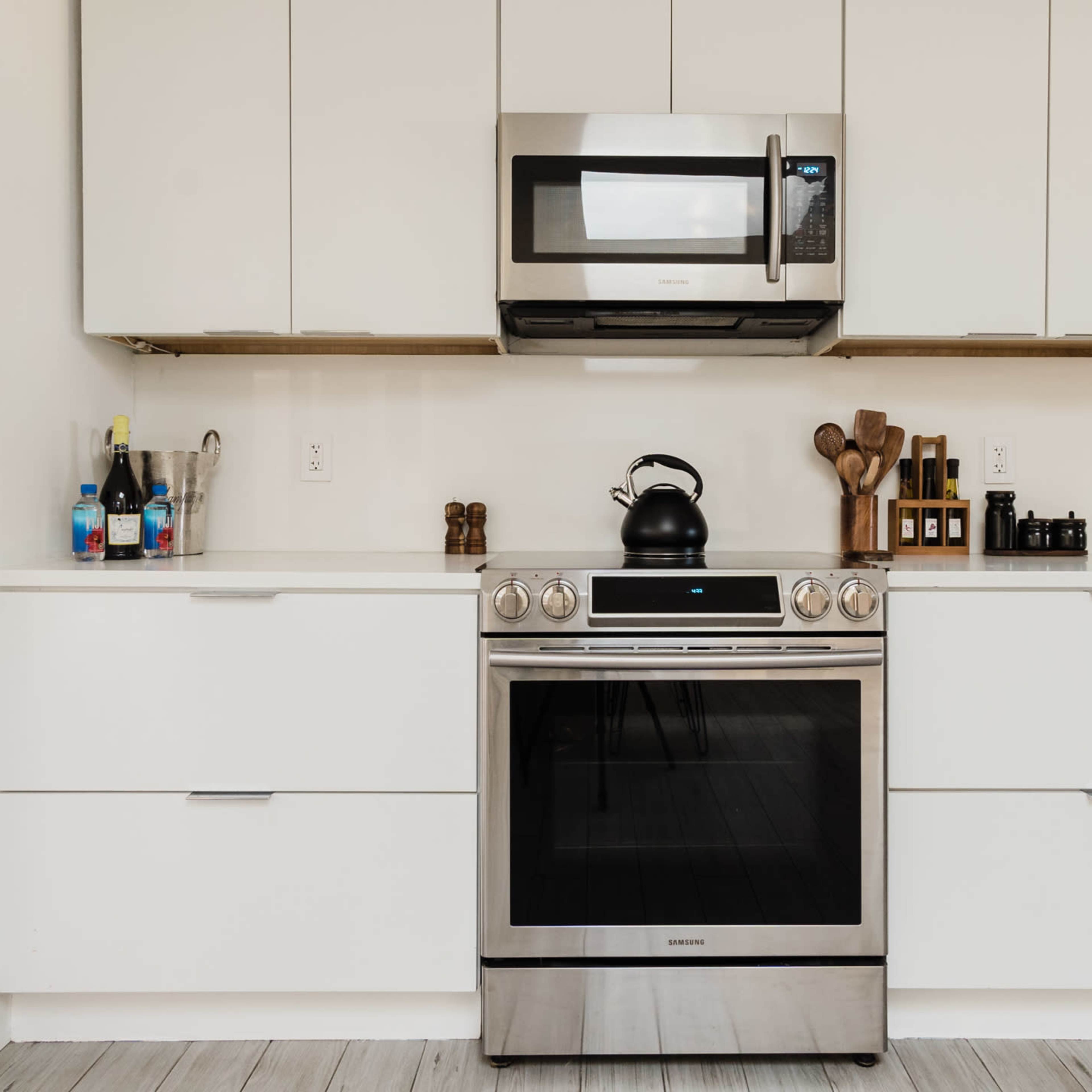 A modern kitchen with stainless steel appliances, including a microwave and stove, and a tidy arrangement of utensils and bottles on the countertop.