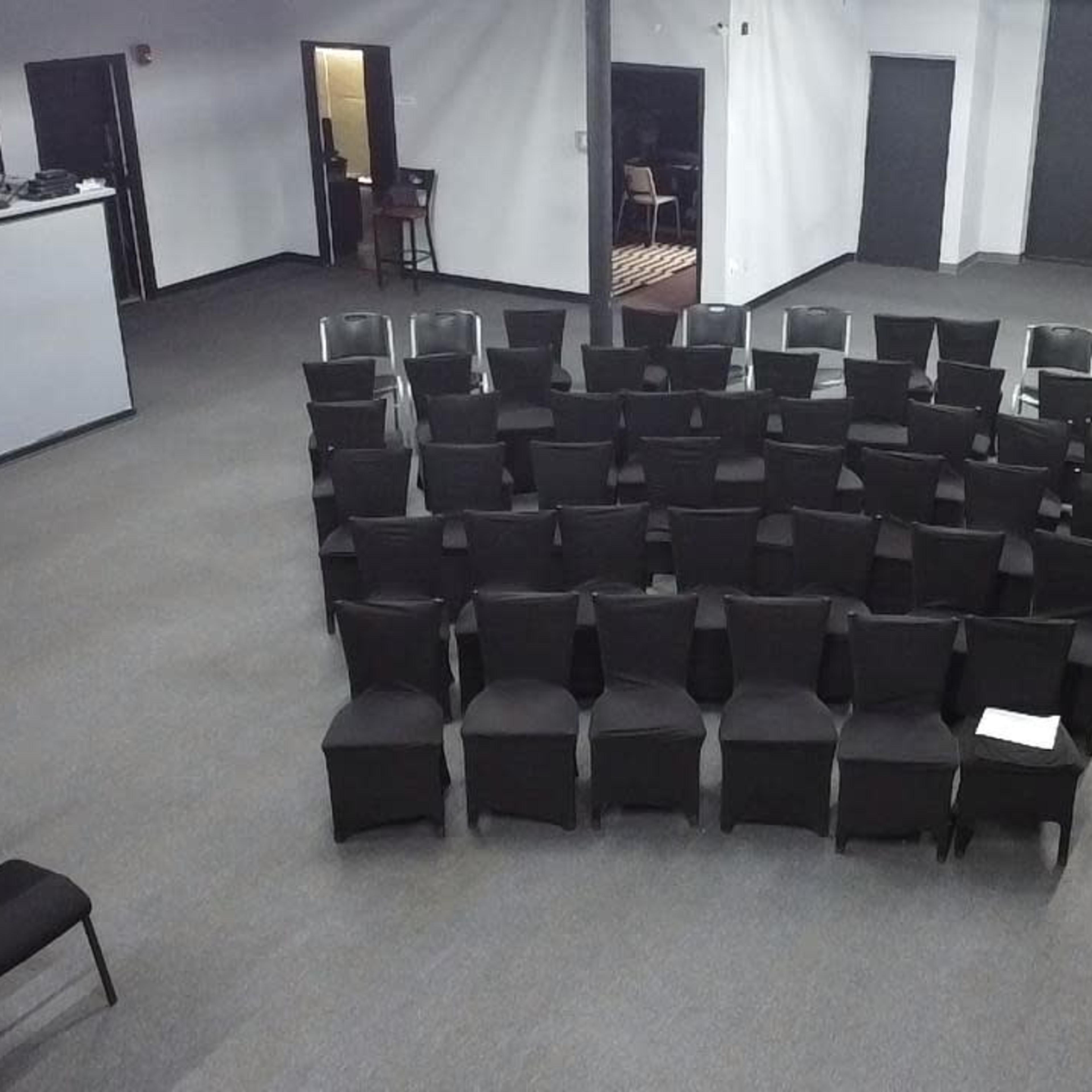A sparsely furnished room with rows of black chairs arranged in a semi-circle facing a stage area.