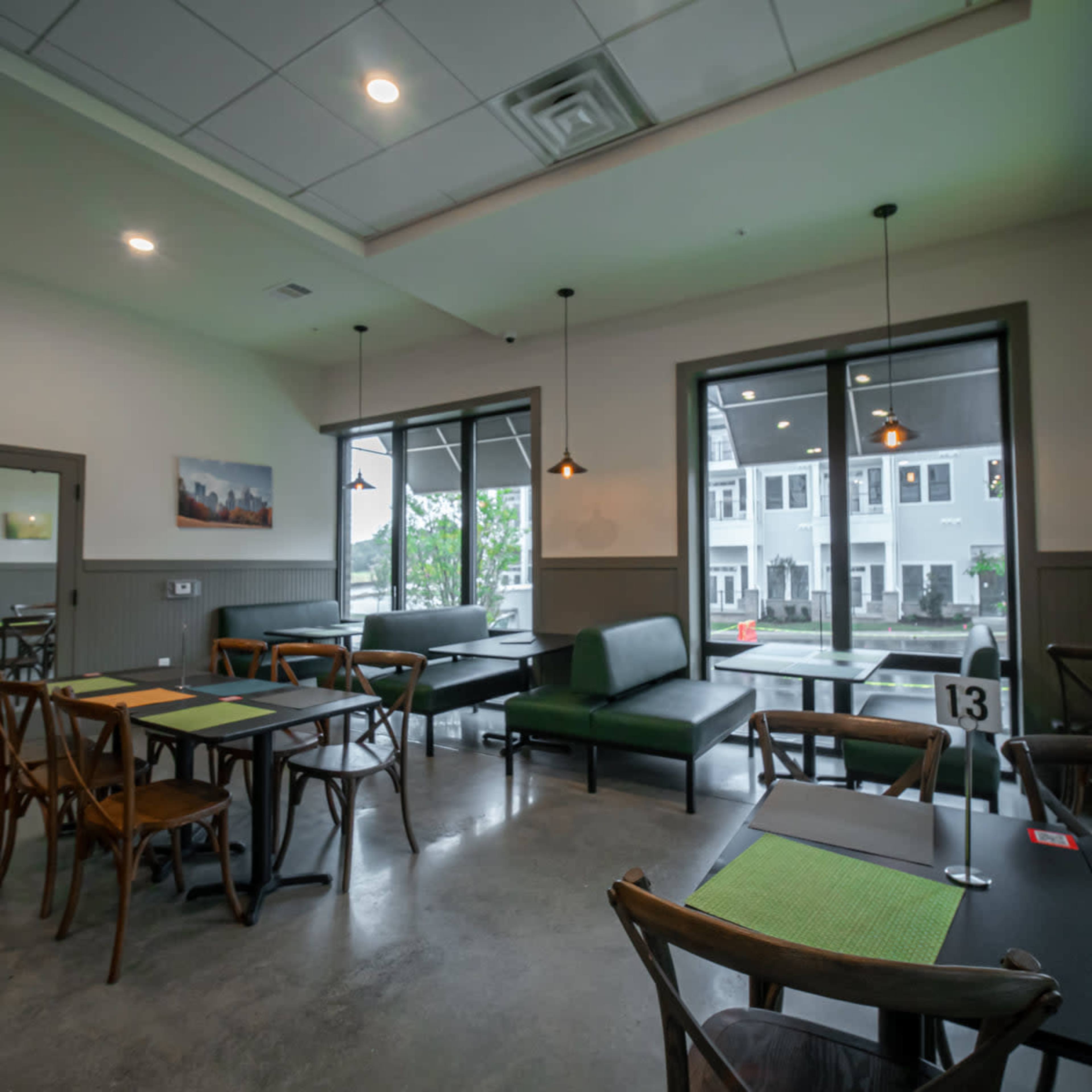 A modern restaurant interior featuring several tables, a green sofa, and large windows allowing natural light.