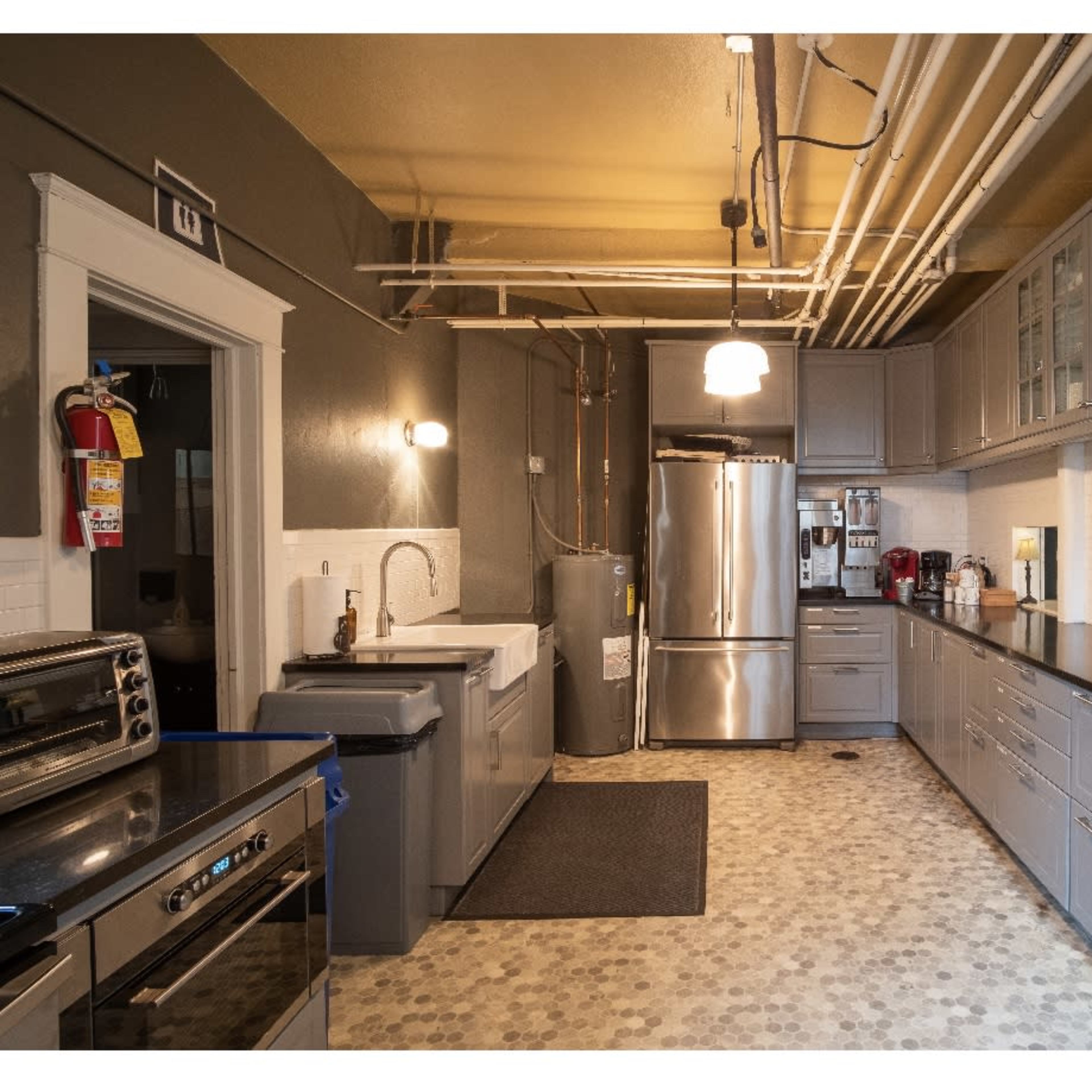 A modern kitchen featuring gray cabinets, stainless steel appliances, a farmhouse sink, and a long counter with a black countertop.