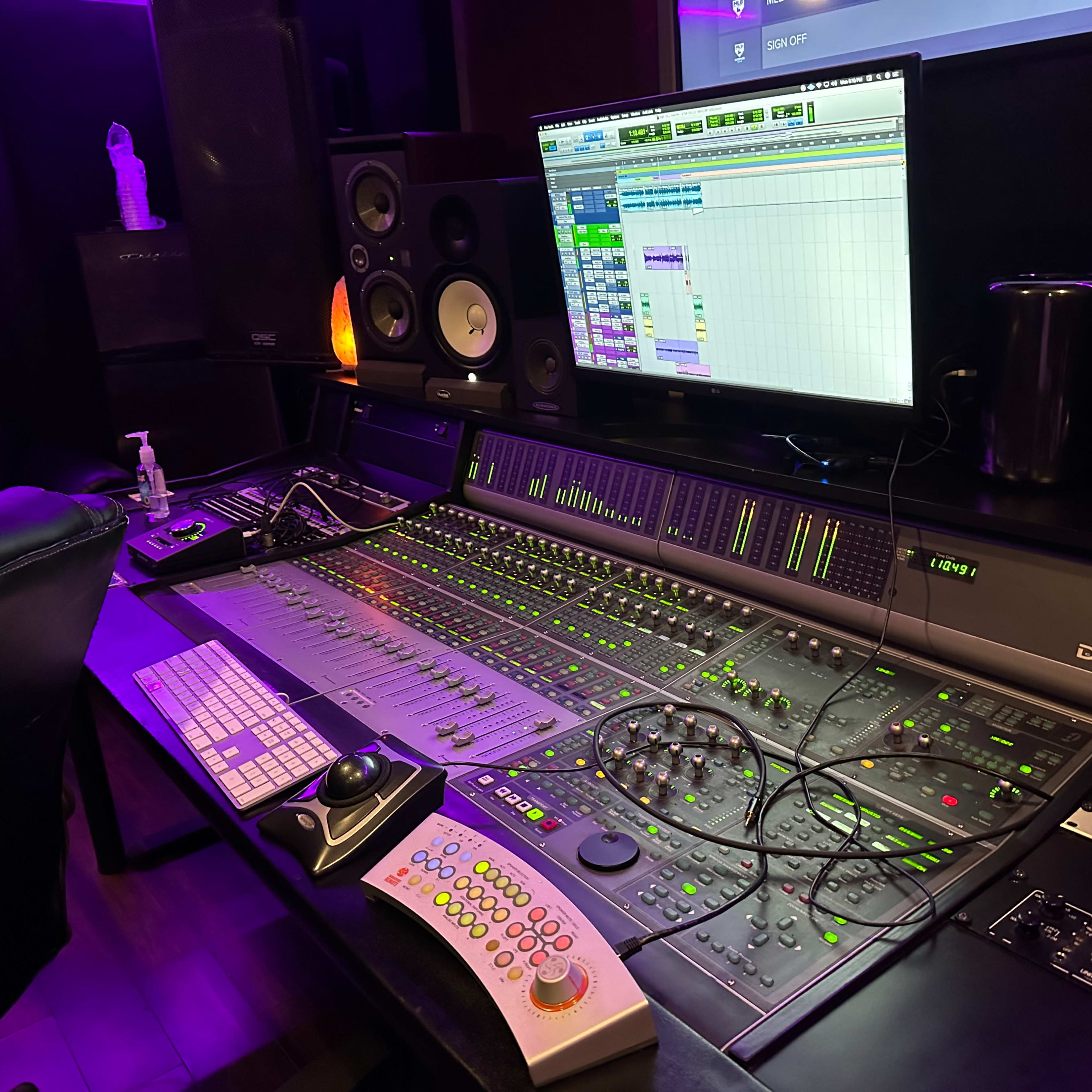 A digital audio workstation with a mixing console, computer screen displaying audio tracks, and various audio equipment in a music studio.