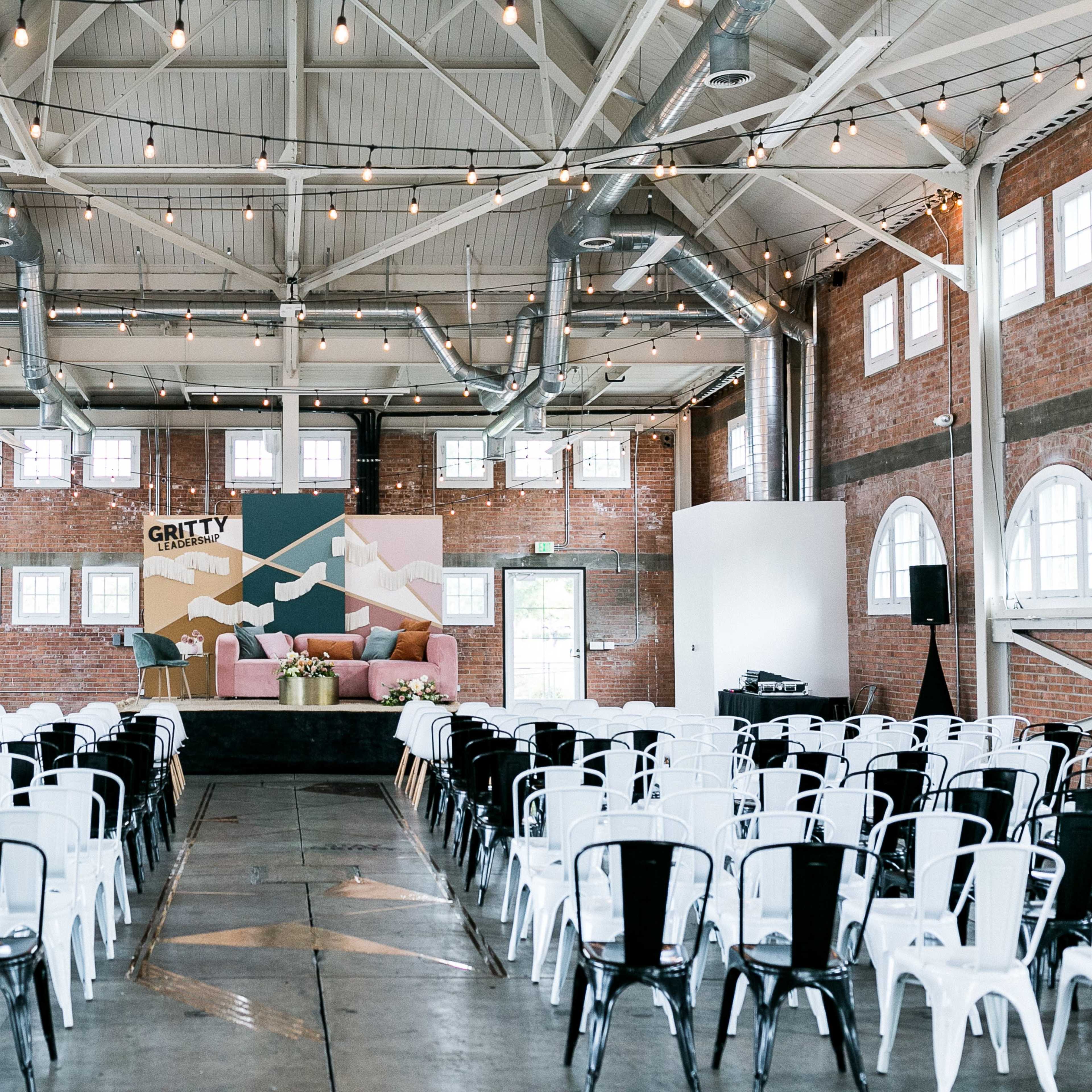 An indoor event space with rows of white and black chairs facing a central stage adorned with a colorful backdrop and couches.
