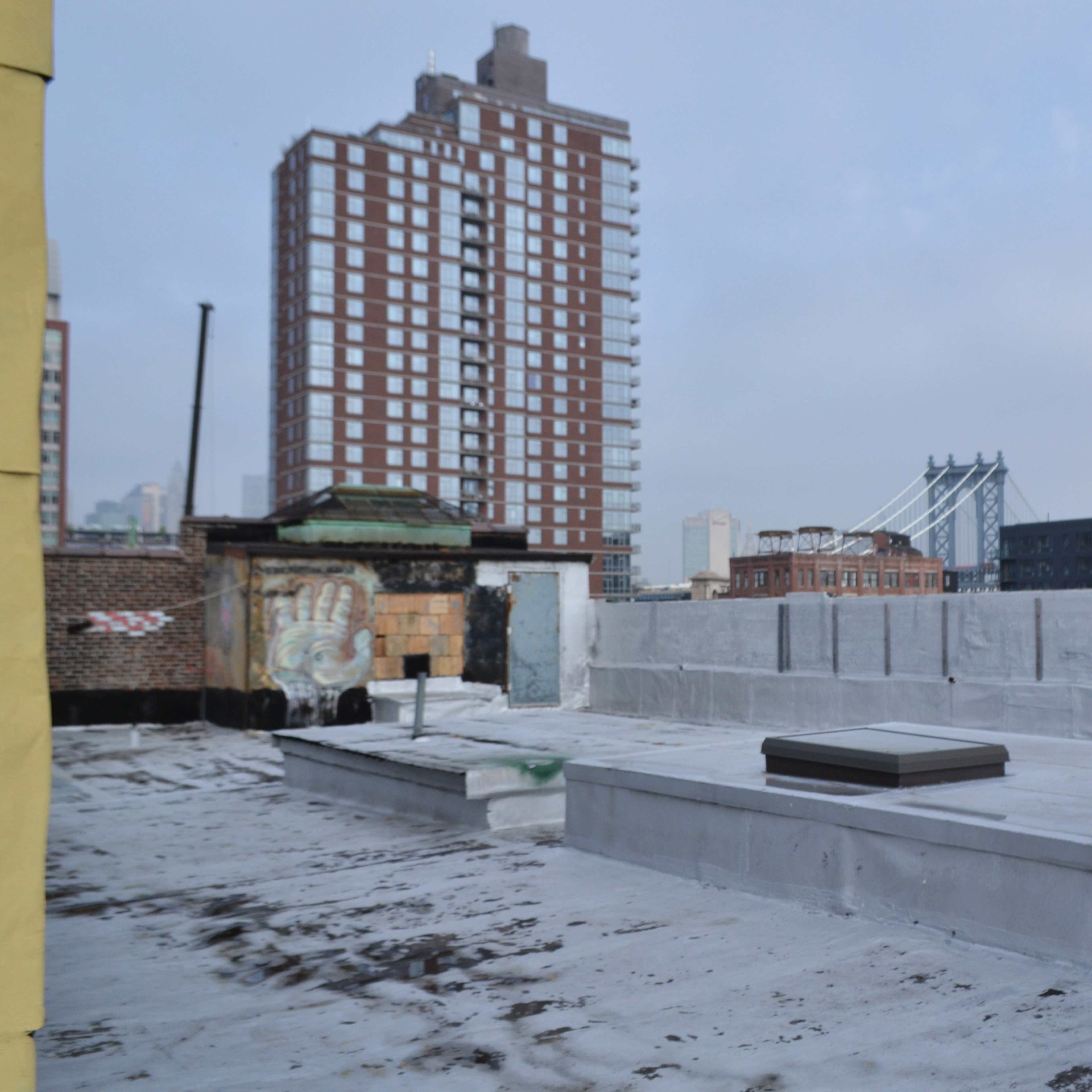 A rooftop area overlooking a city skyline with buildings and a bridge in the background.