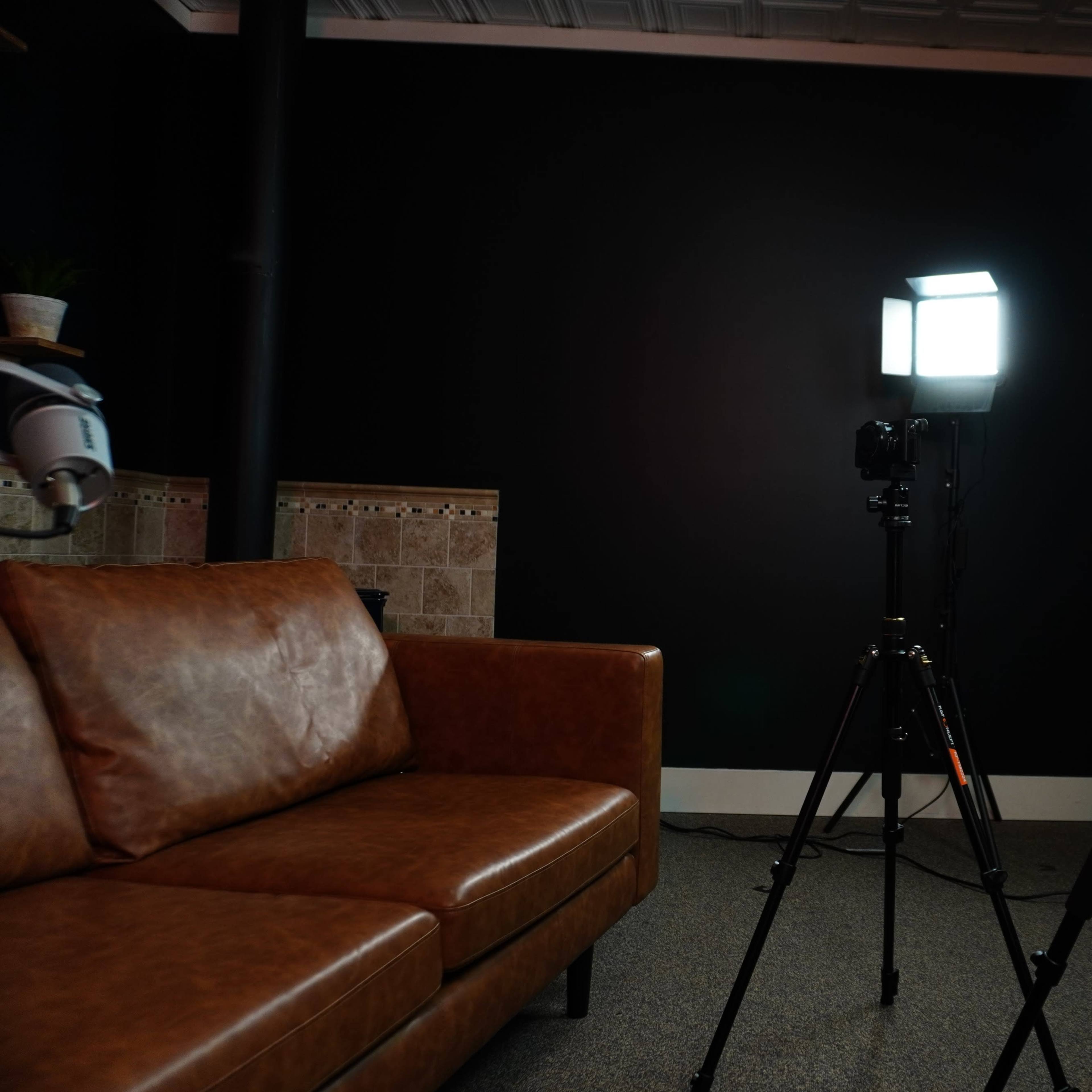 A brown leather sofa positioned next to two studio lights on tripods, with a black wall in the background.