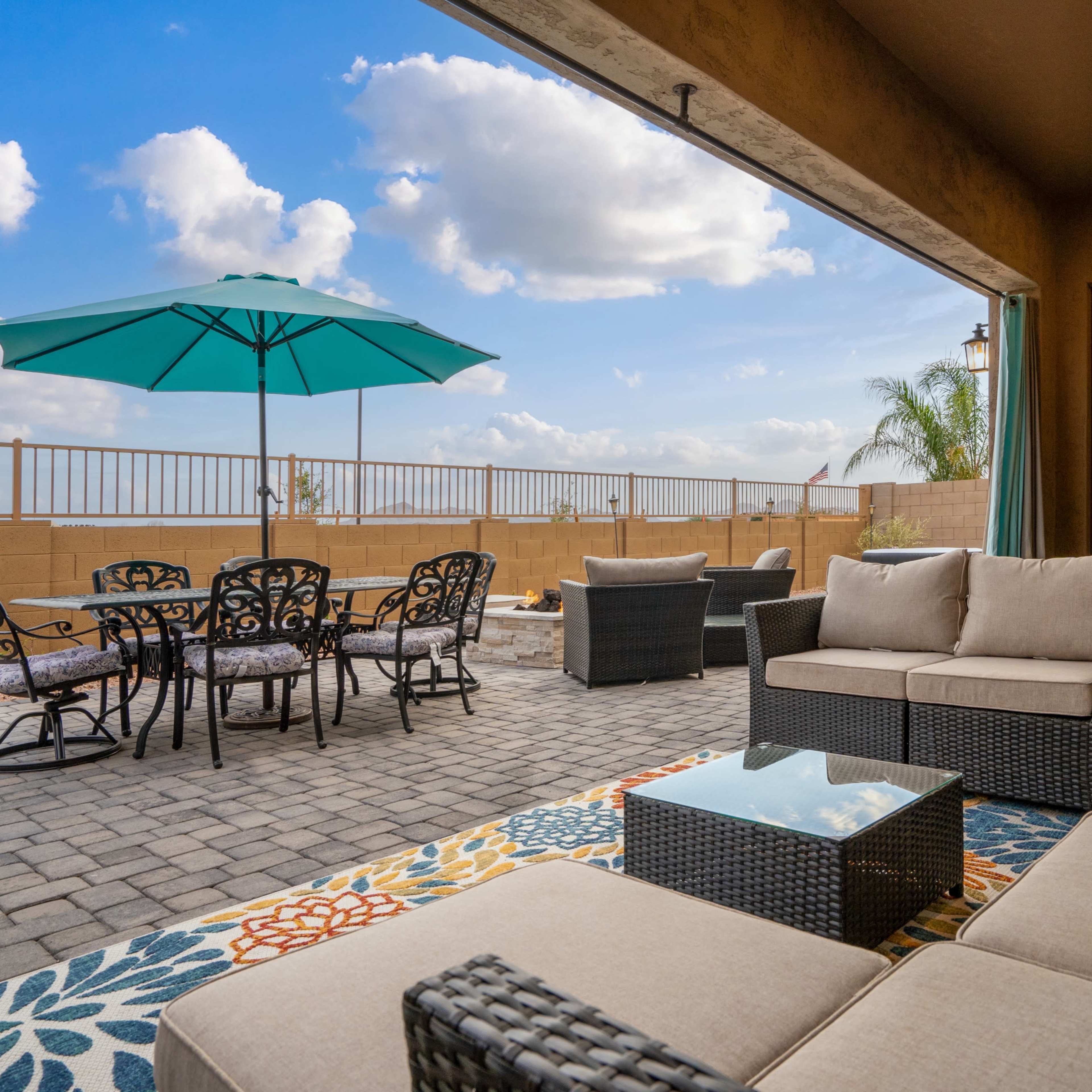 A patio area features a seating arrangement with cushions, a table, and an umbrella, overlooking a fenced backyard.
