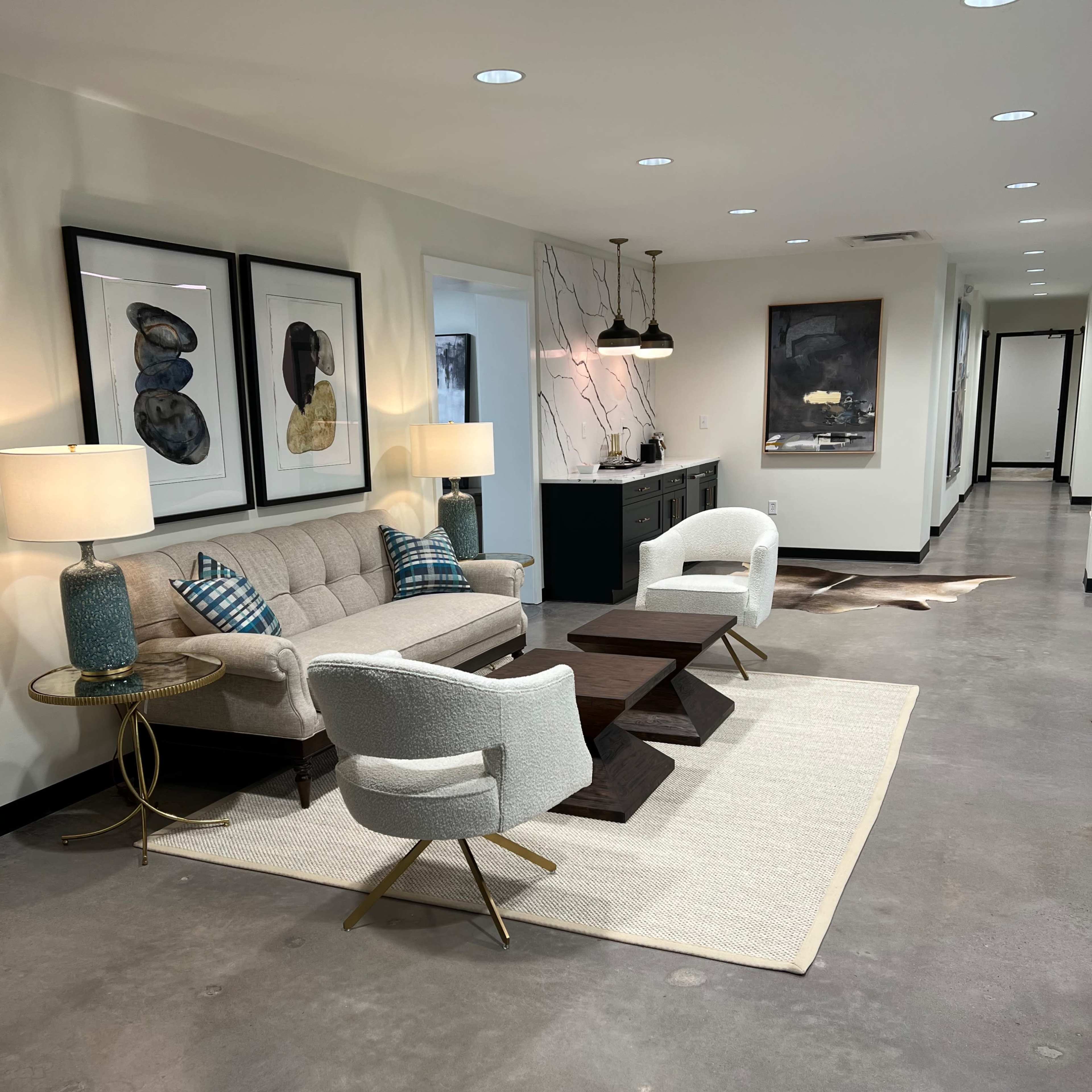 A modern hallway featuring a couch, two armchairs, a coffee table, and decorative wall art, illuminated by overhead lighting.
