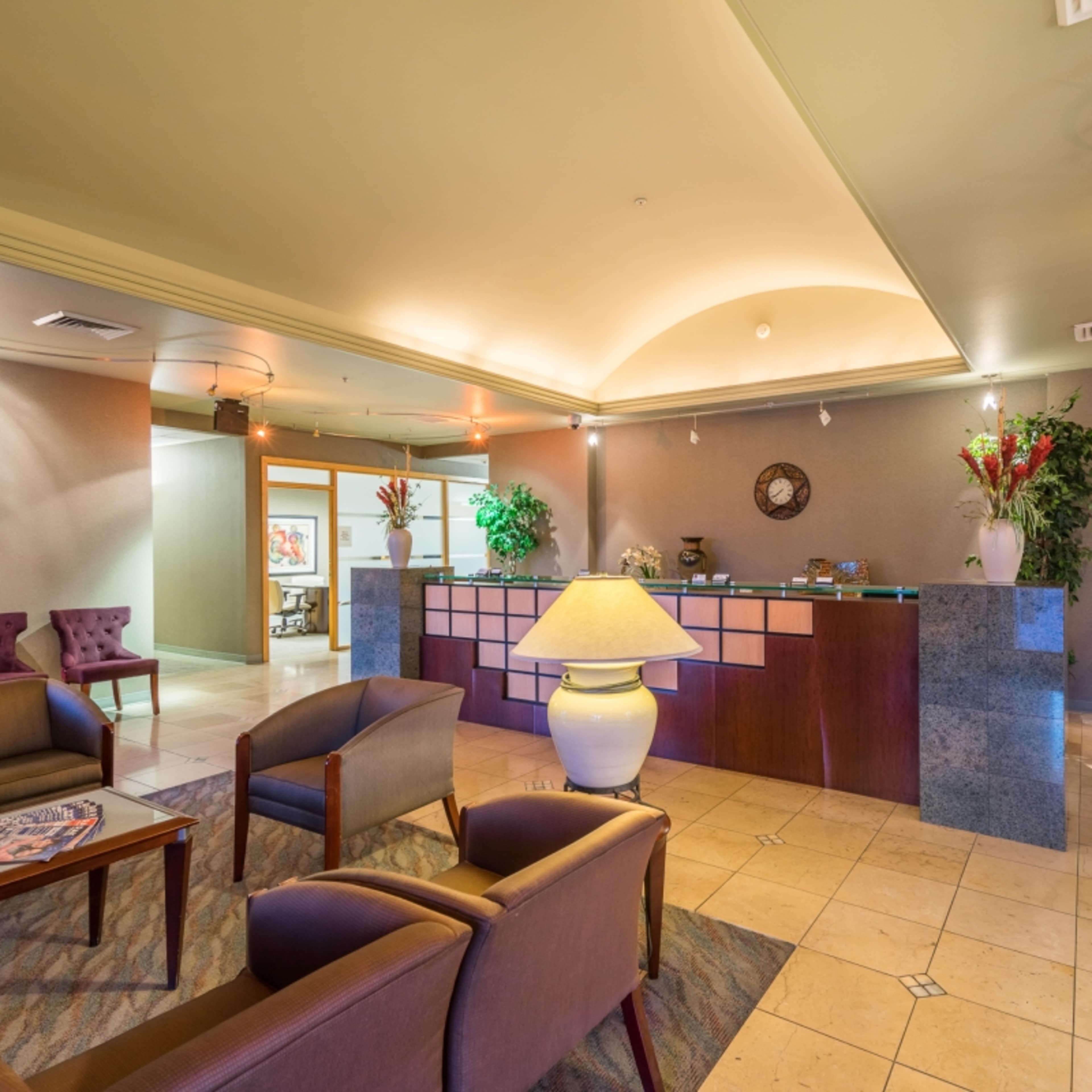 A lobby with a reception desk, seating area with chairs, and decorative plants.