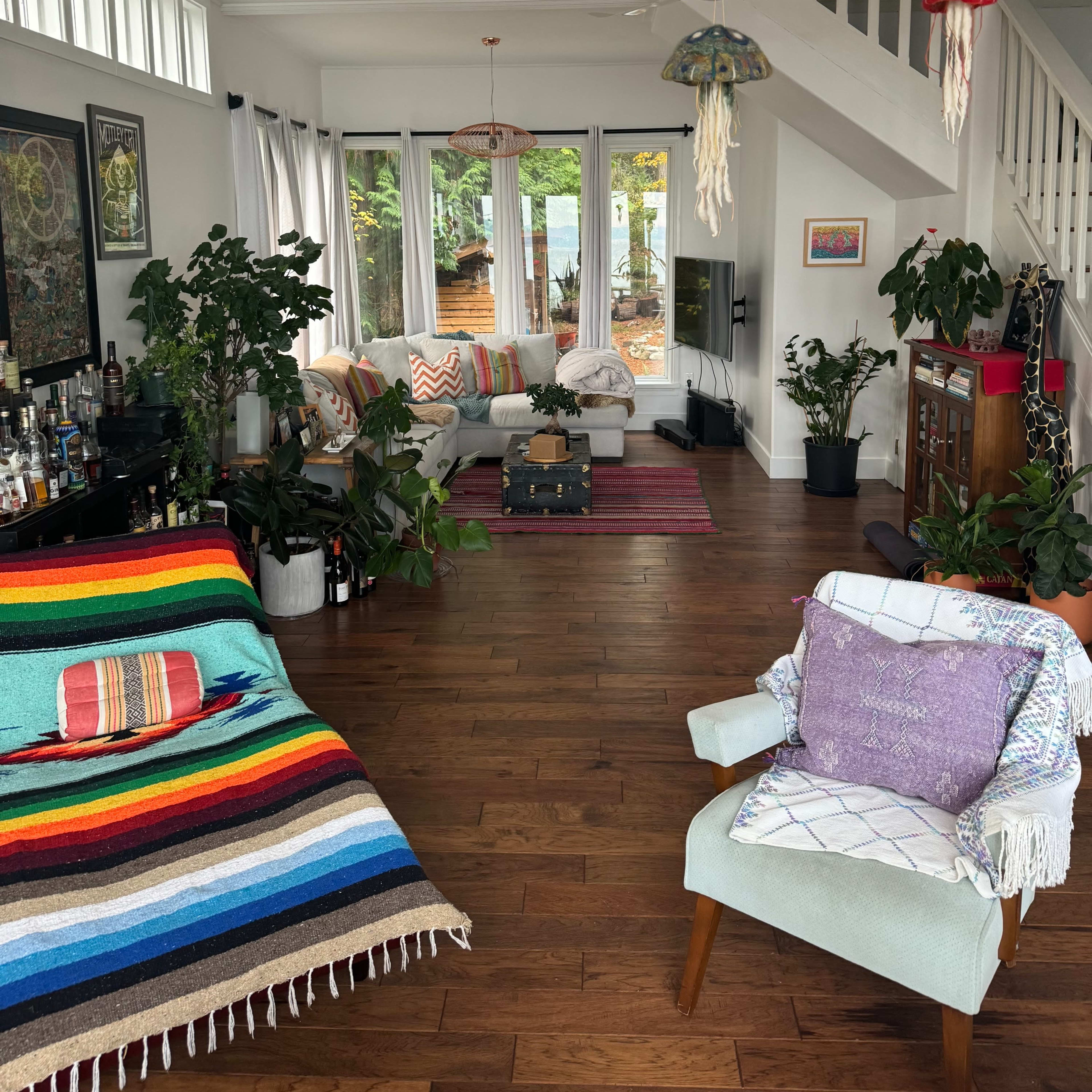 A living room features a striped blanket draped over a sofa, potted plants, and colorful pendant lights hanging from the ceiling.