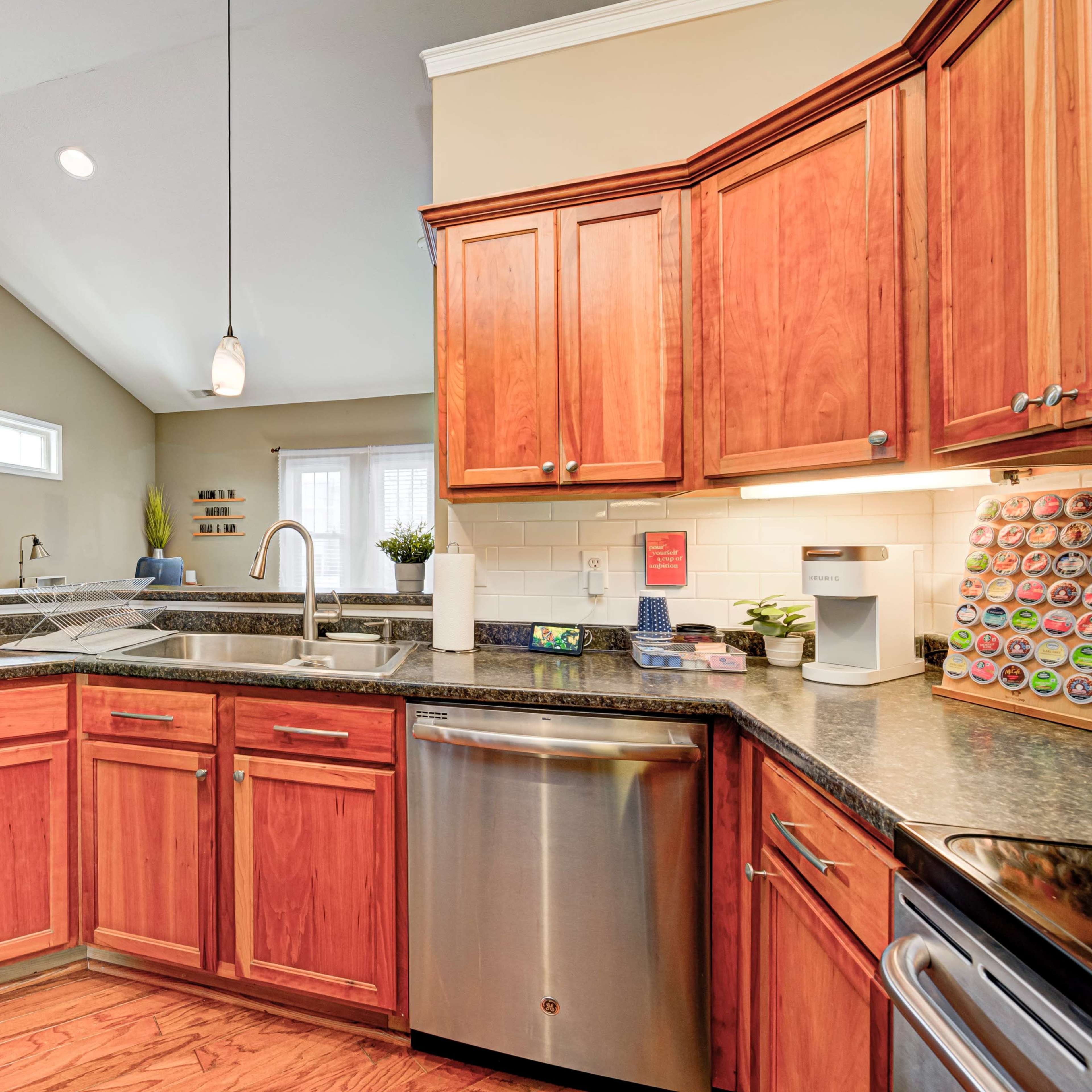 A modern kitchen features wooden cabinetry, a stainless steel dishwasher, and a countertop with various kitchen appliances and utensils.