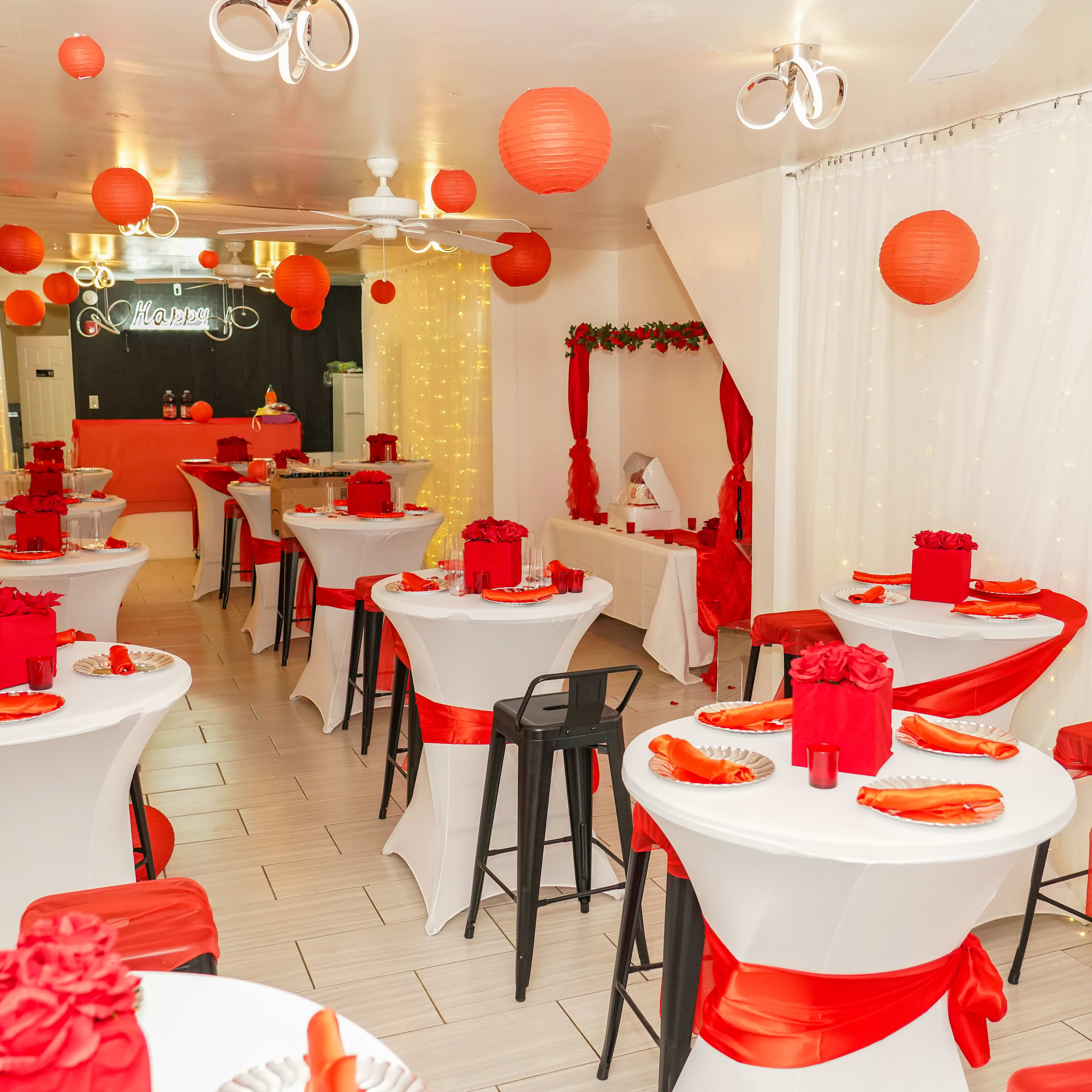 The interior of a decorated dining space features red and white tables with floral arrangements and hanging paper lanterns.