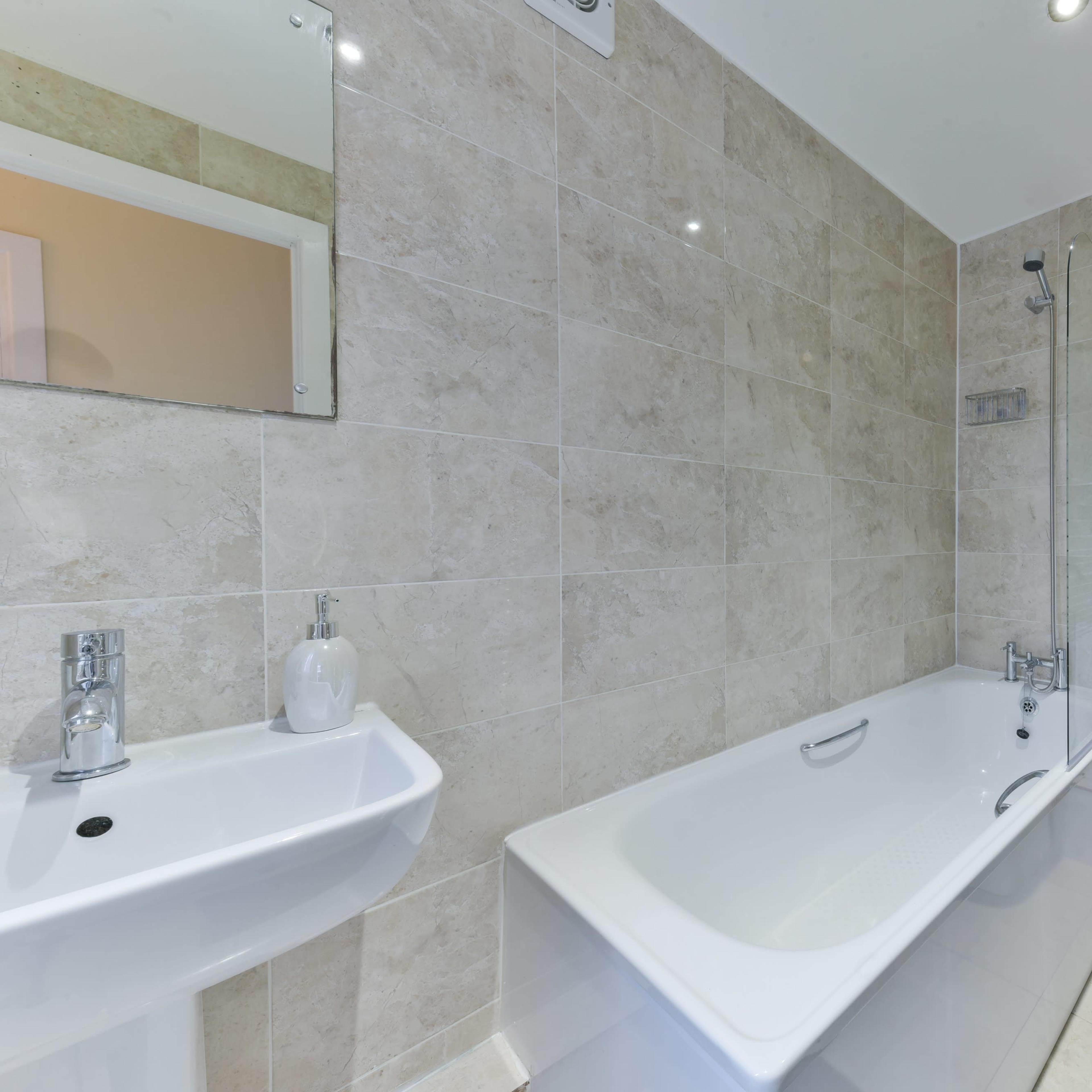 A modern bathroom featuring a bathtub, a shower, a sink, and a toilet, all surrounded by textured tile walls.