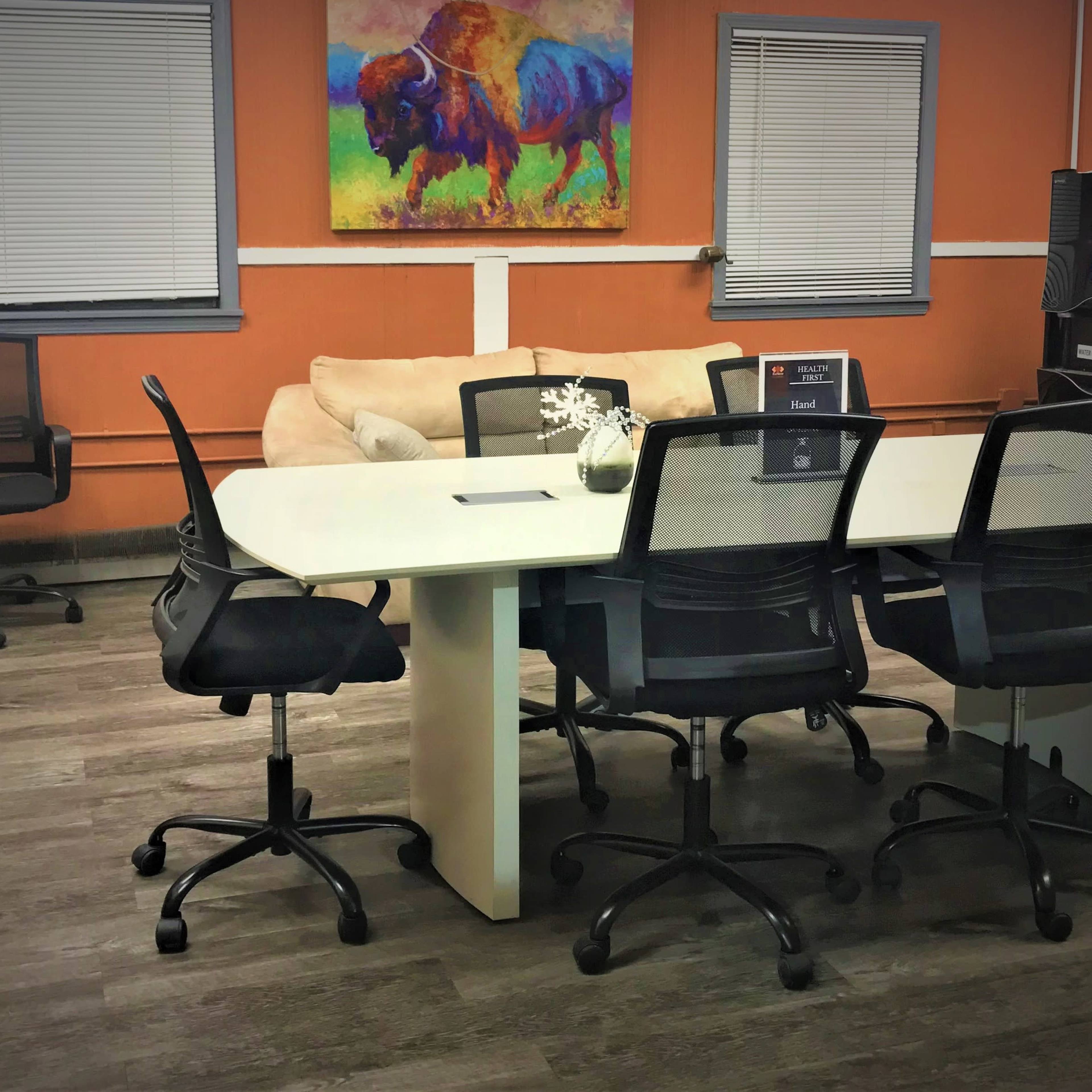 A meeting room with a large white table surrounded by black chairs, a beige couch in the background, and an abstract painting of a buffalo on the wall.