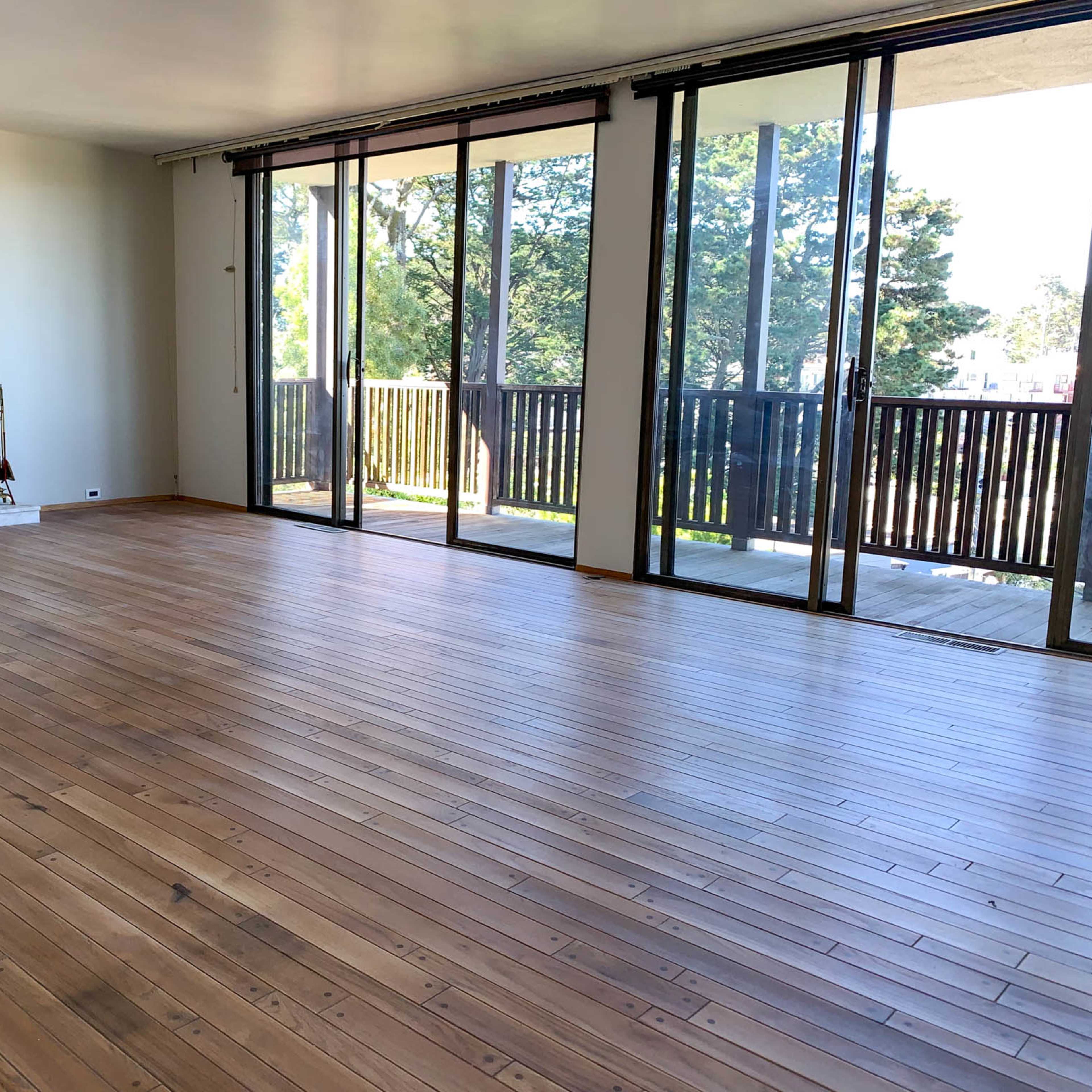 A spacious room with wooden floors, large windows, and a fireplace against a white marble wall.