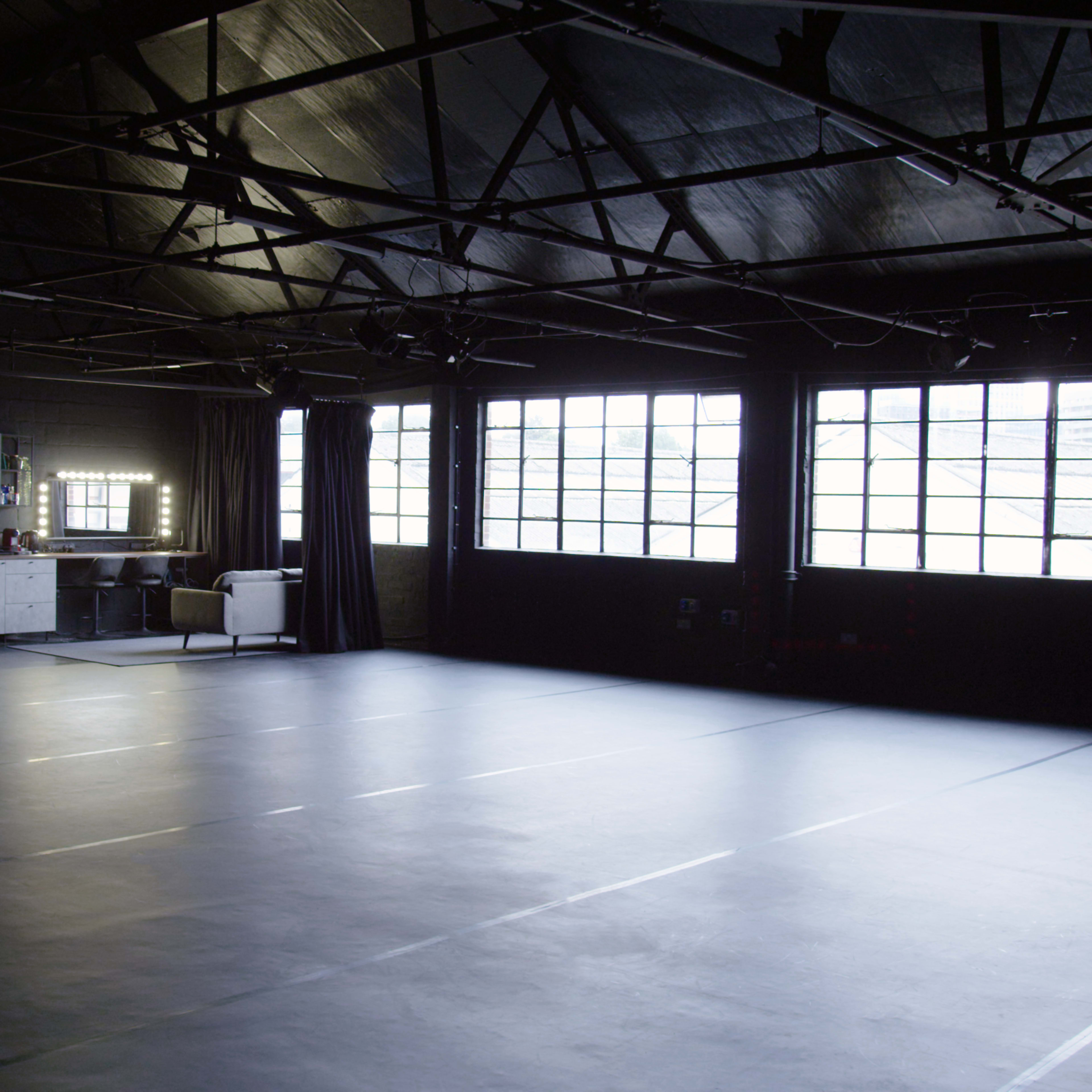 A spacious, dimly lit studio with large windows and a row of mirrors against one wall.