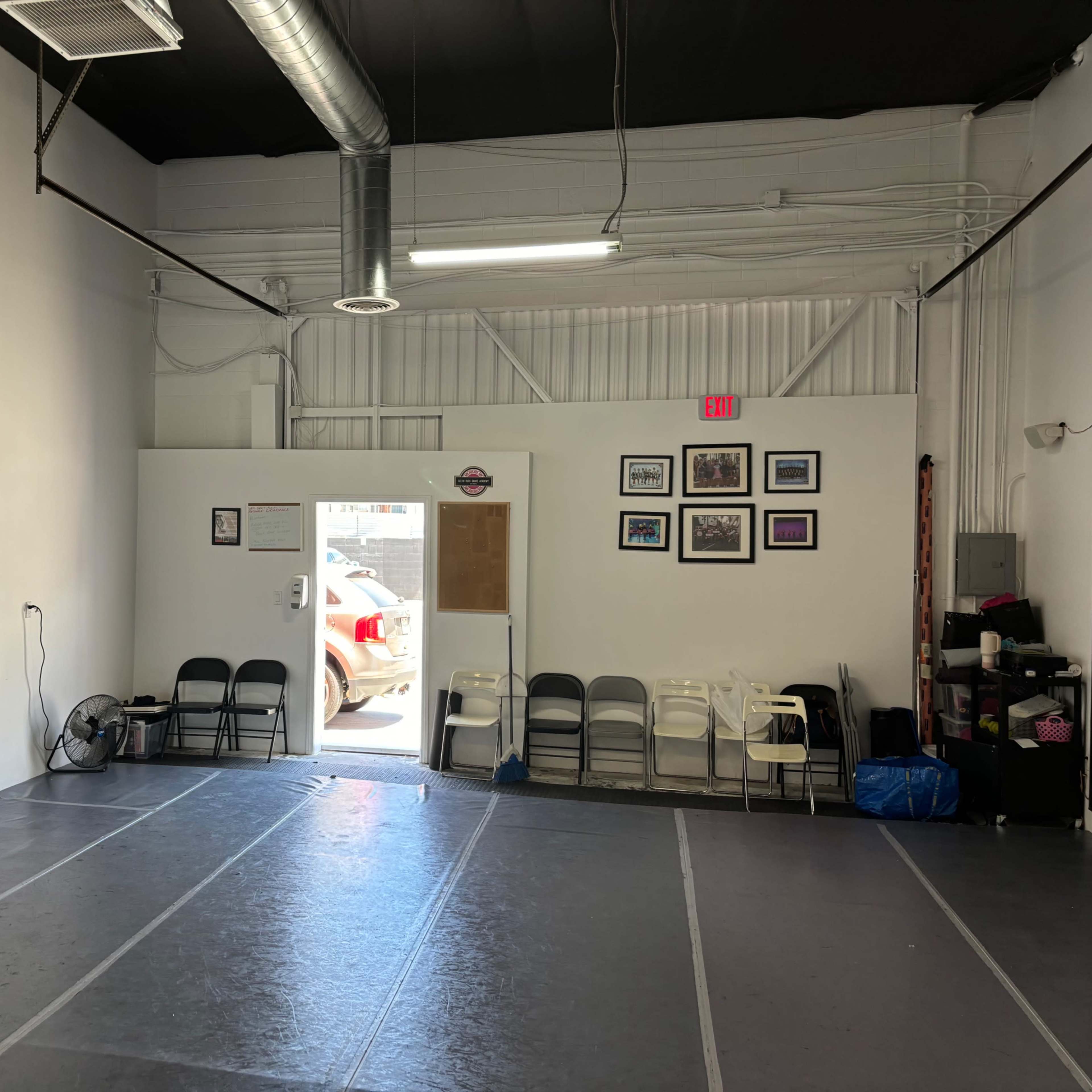 An empty indoor space with gray flooring, a door leading outside, and a row of chairs against one wall.
