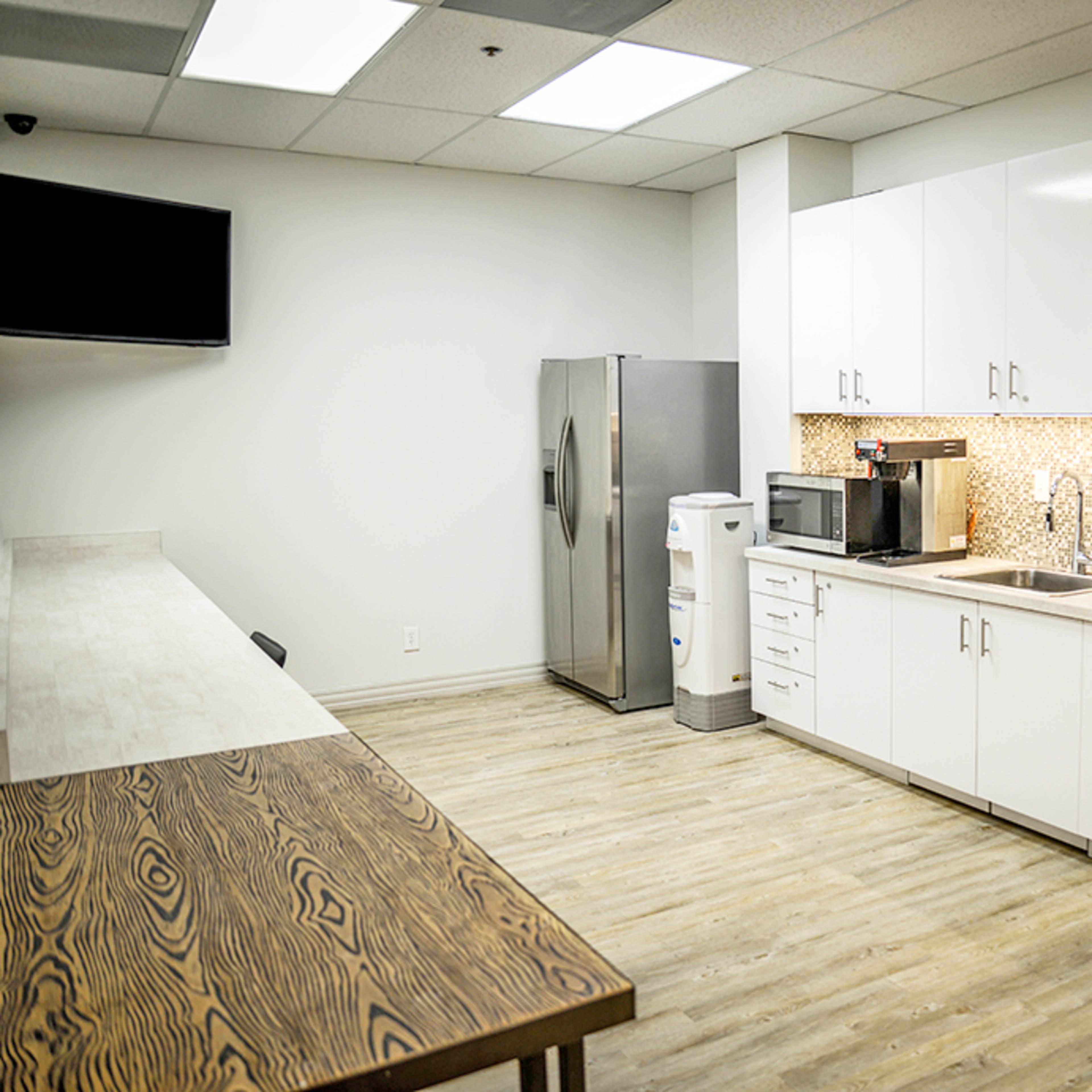 A modern break room featuring a refrigerator, microwave, sink, and a wooden table with chairs.