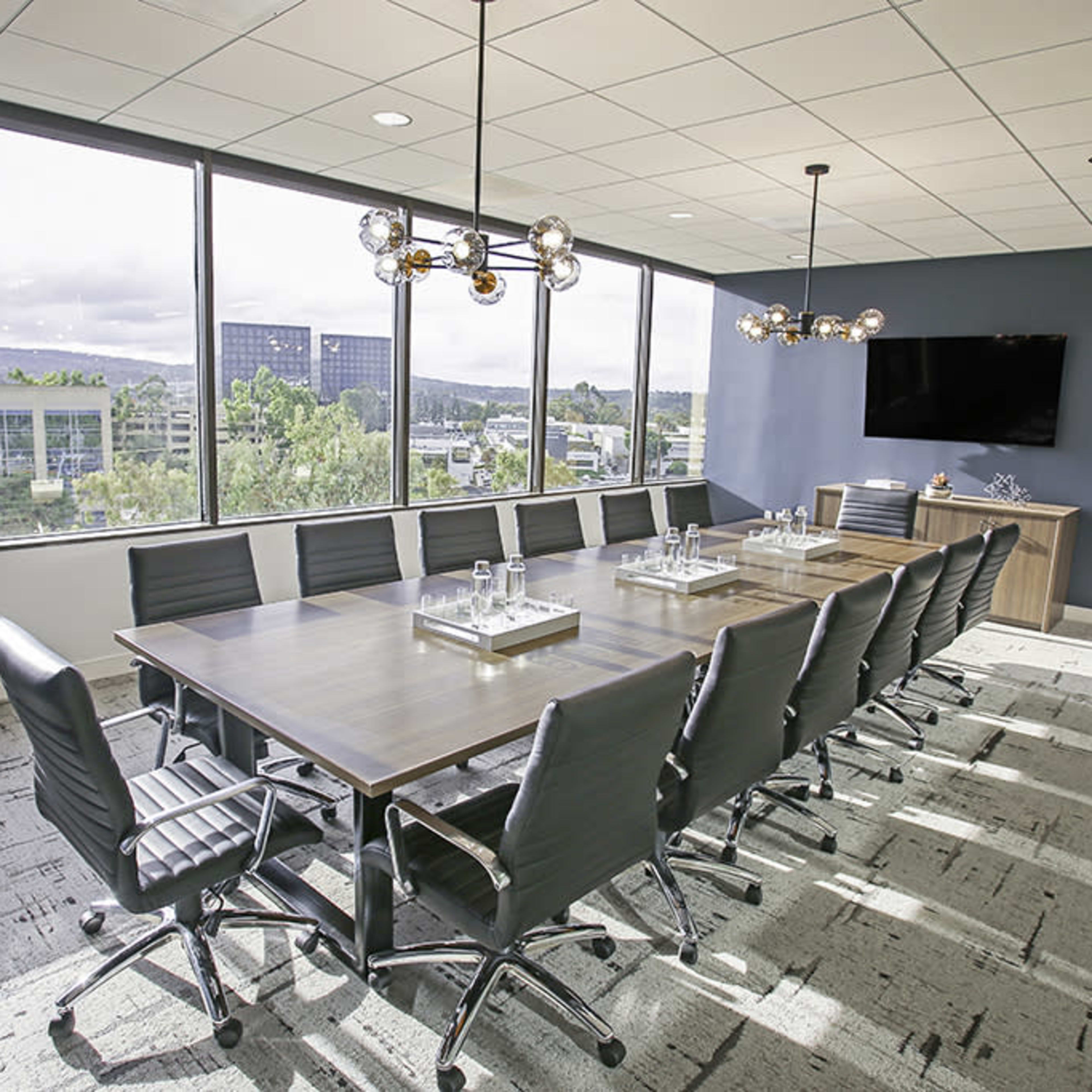 A modern conference room features a large table surrounded by black leather chairs, with large windows providing a view of the outdoors.