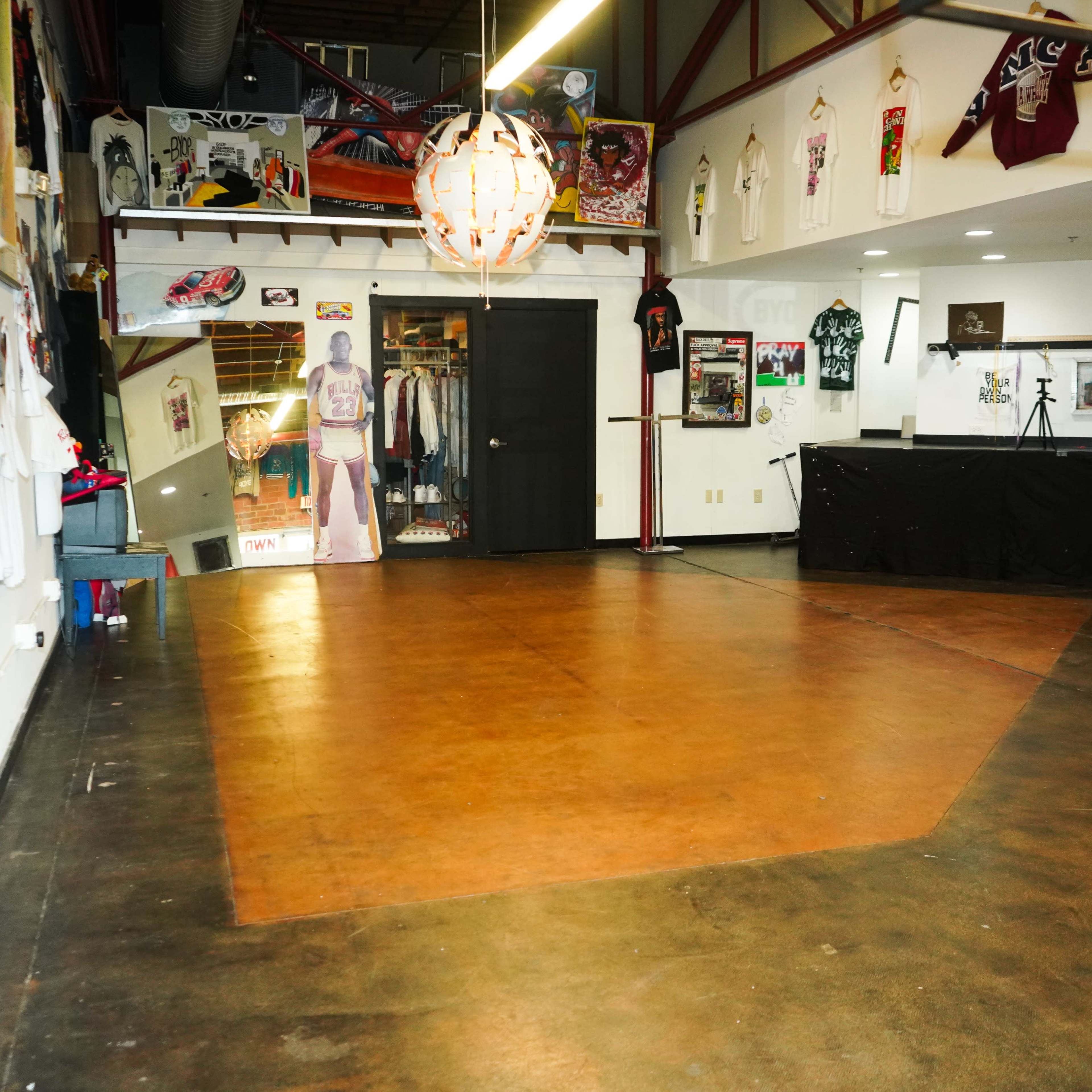 A spacious room with polished concrete flooring, decorated with various shirts and artwork on the walls, and containing a black counter along one side.