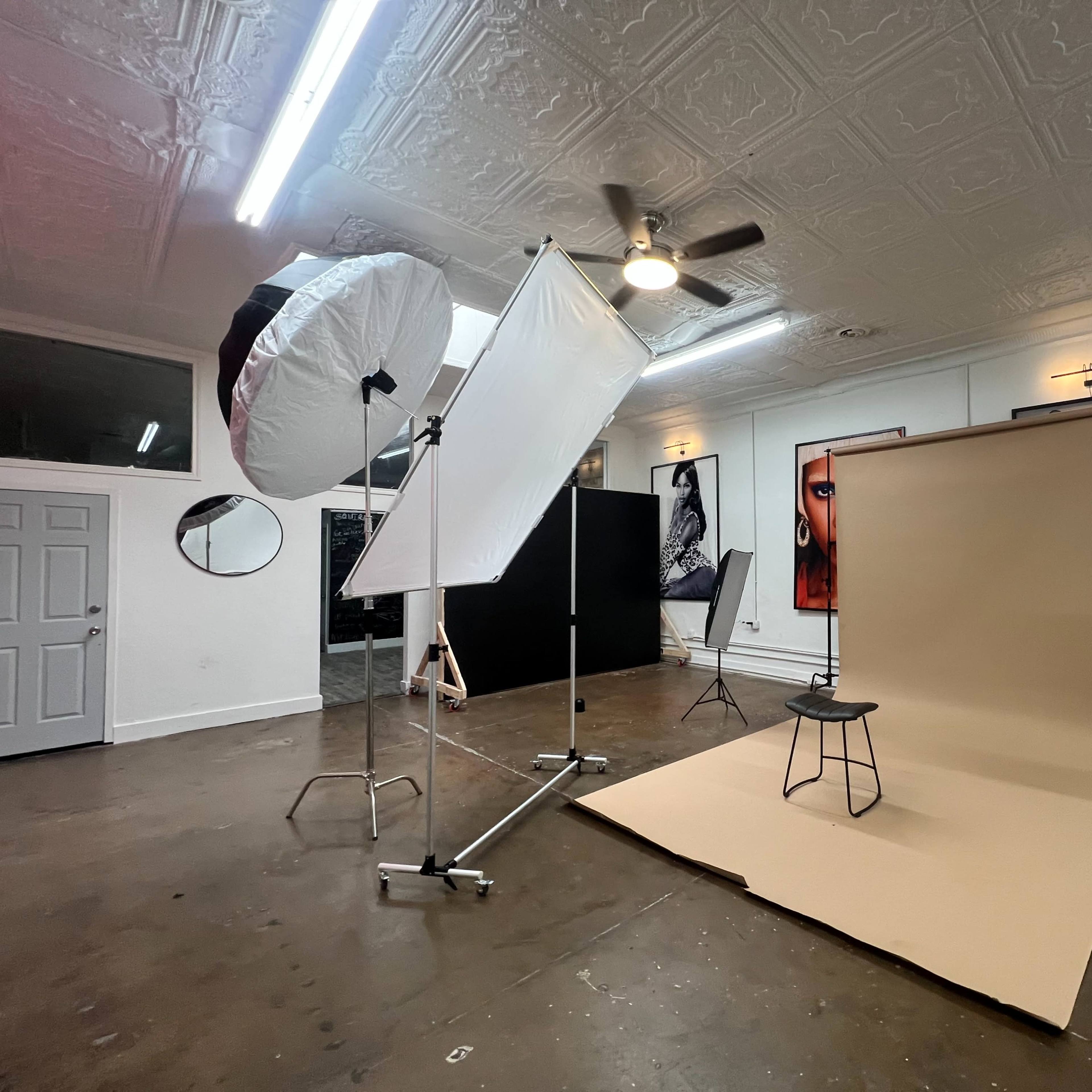A photography studio set up with a neutral backdrop, various lighting equipment, and a chair positioned in the center.