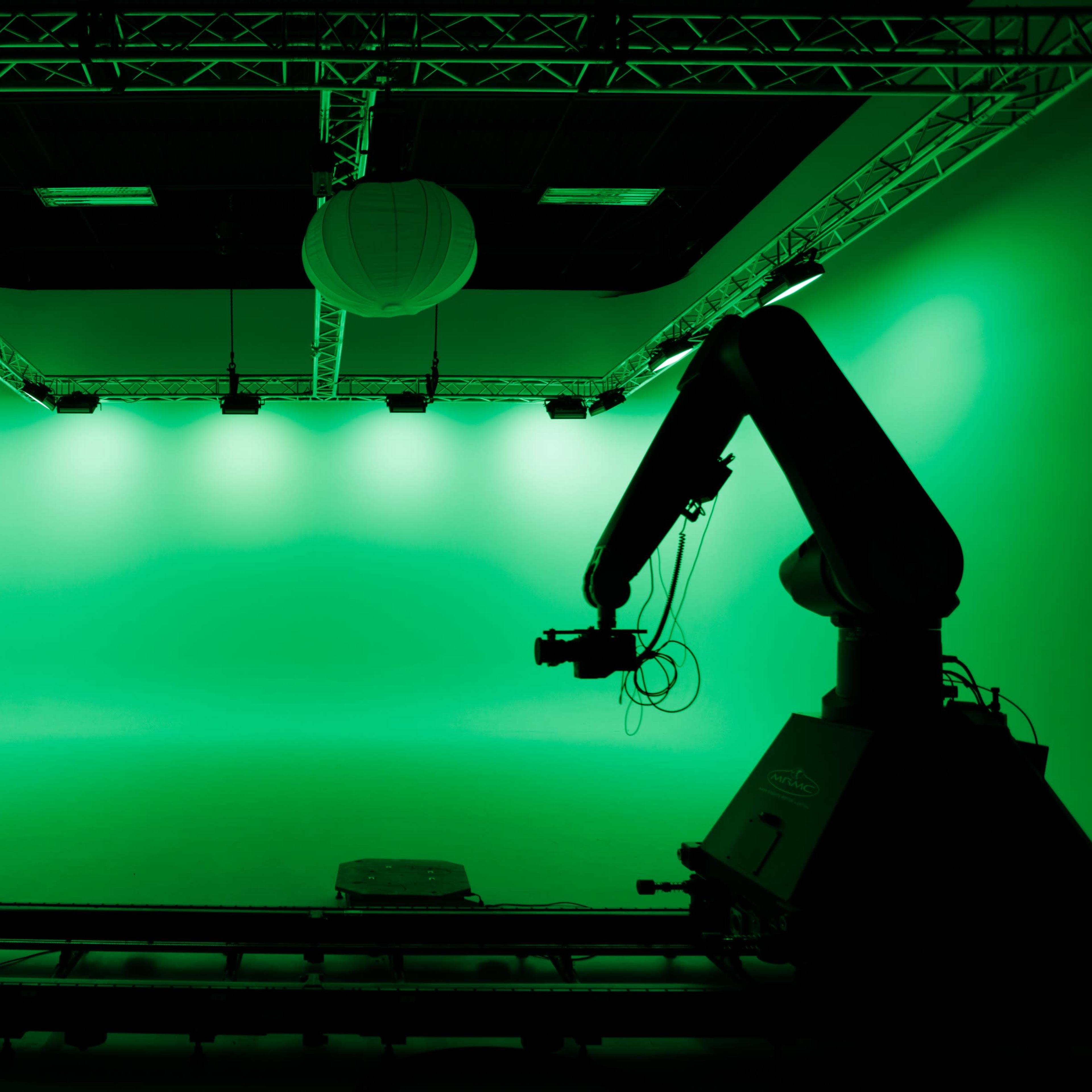 A green screen studio with a robotic arm positioned on a track beneath overhead lighting.