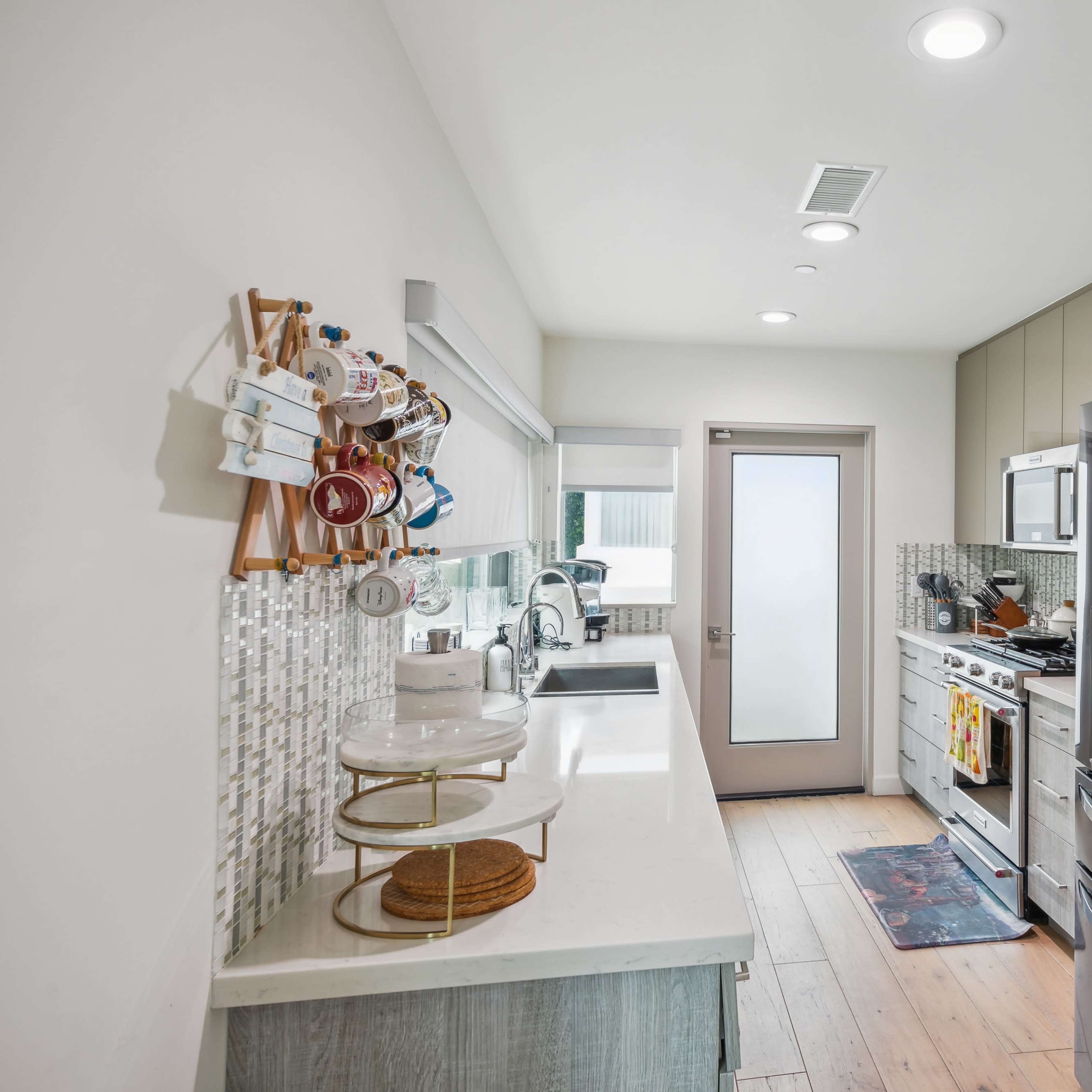 A modern kitchen with stainless steel appliances, a white countertop, and a tile backsplash, featuring a door leading outside.