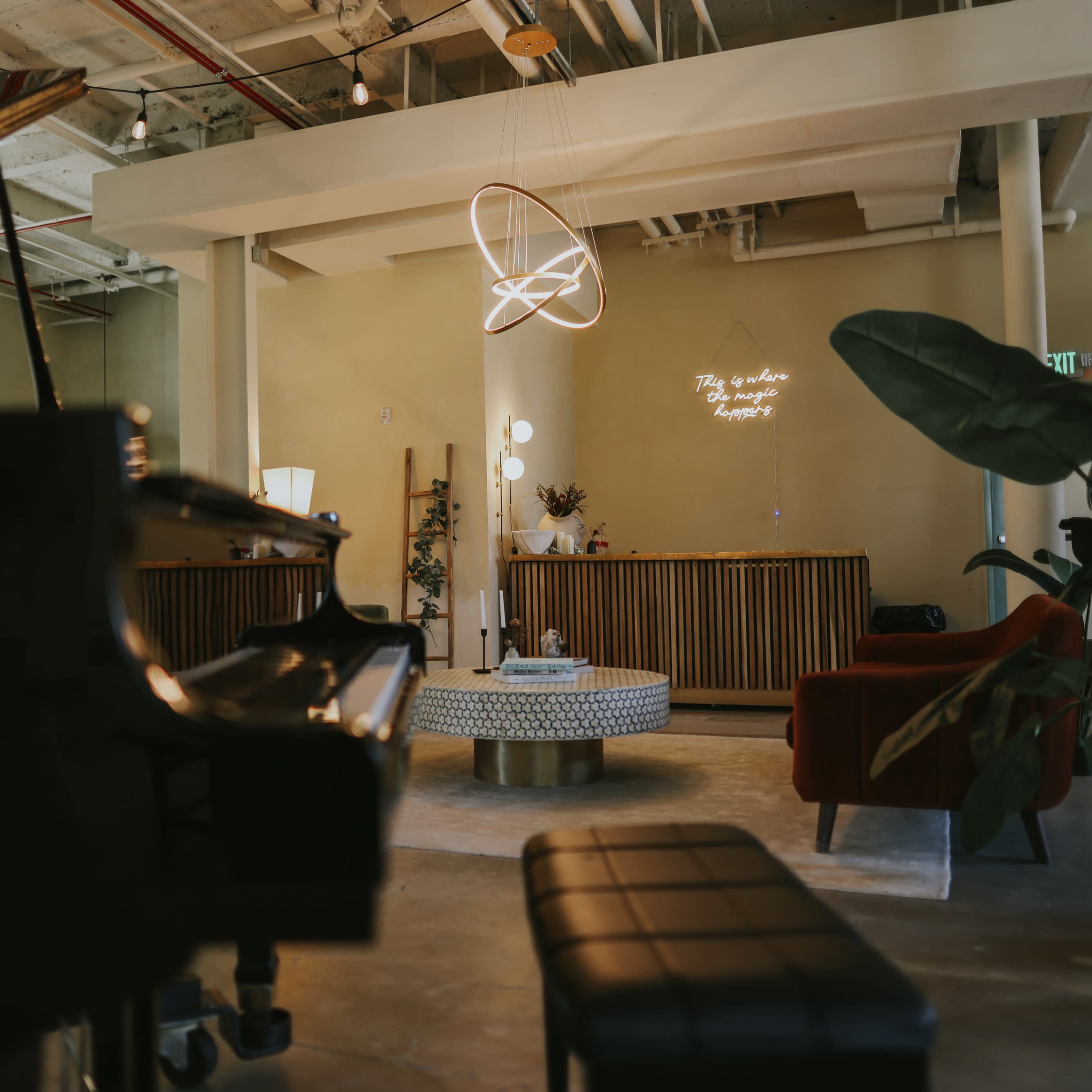 A spacious indoor lounge features a grand piano, a circular coffee table, and modern decor with a pendant light hanging above.