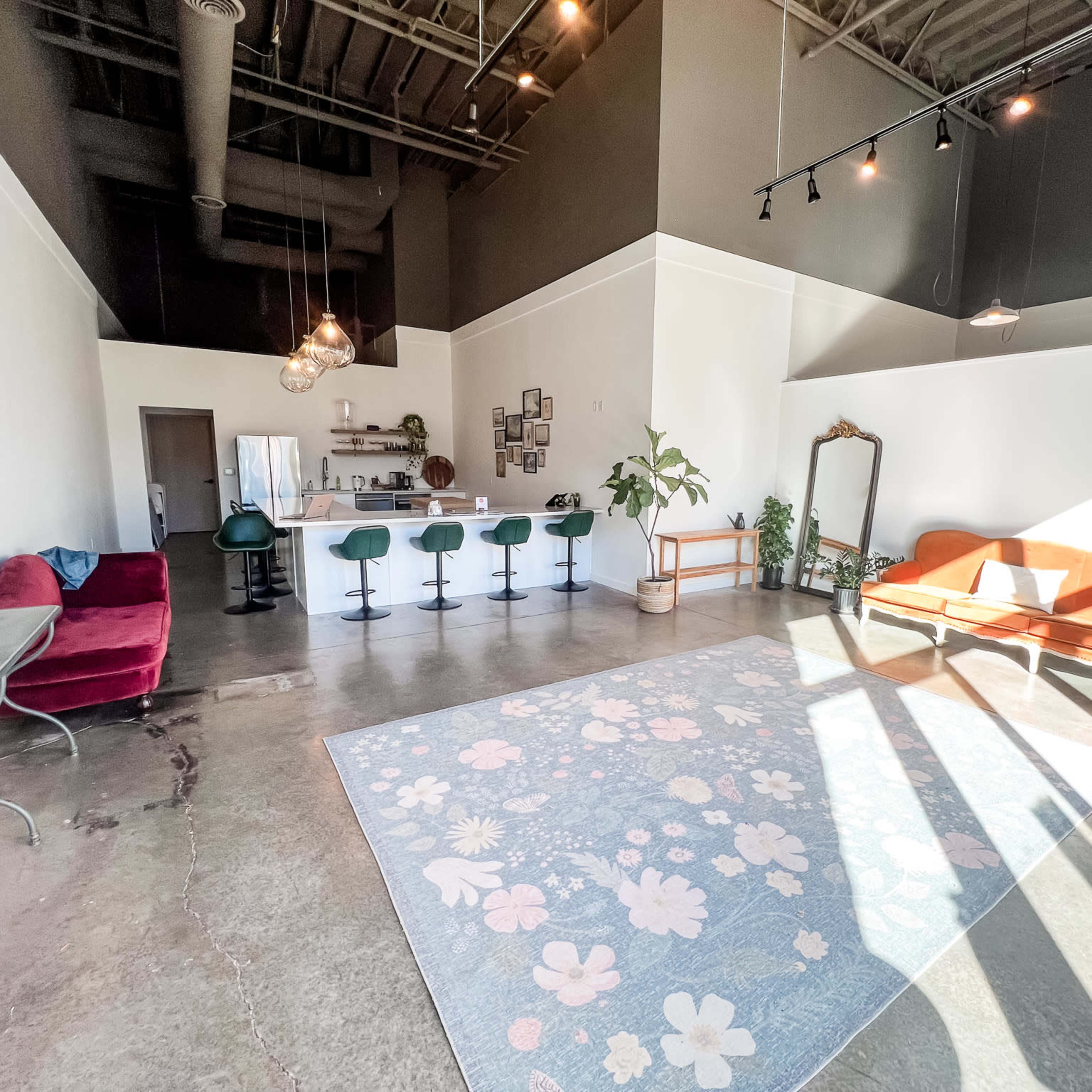 An open, modern interior space with a seating area, a bar counter with stools, and large windows allowing natural light to enter.