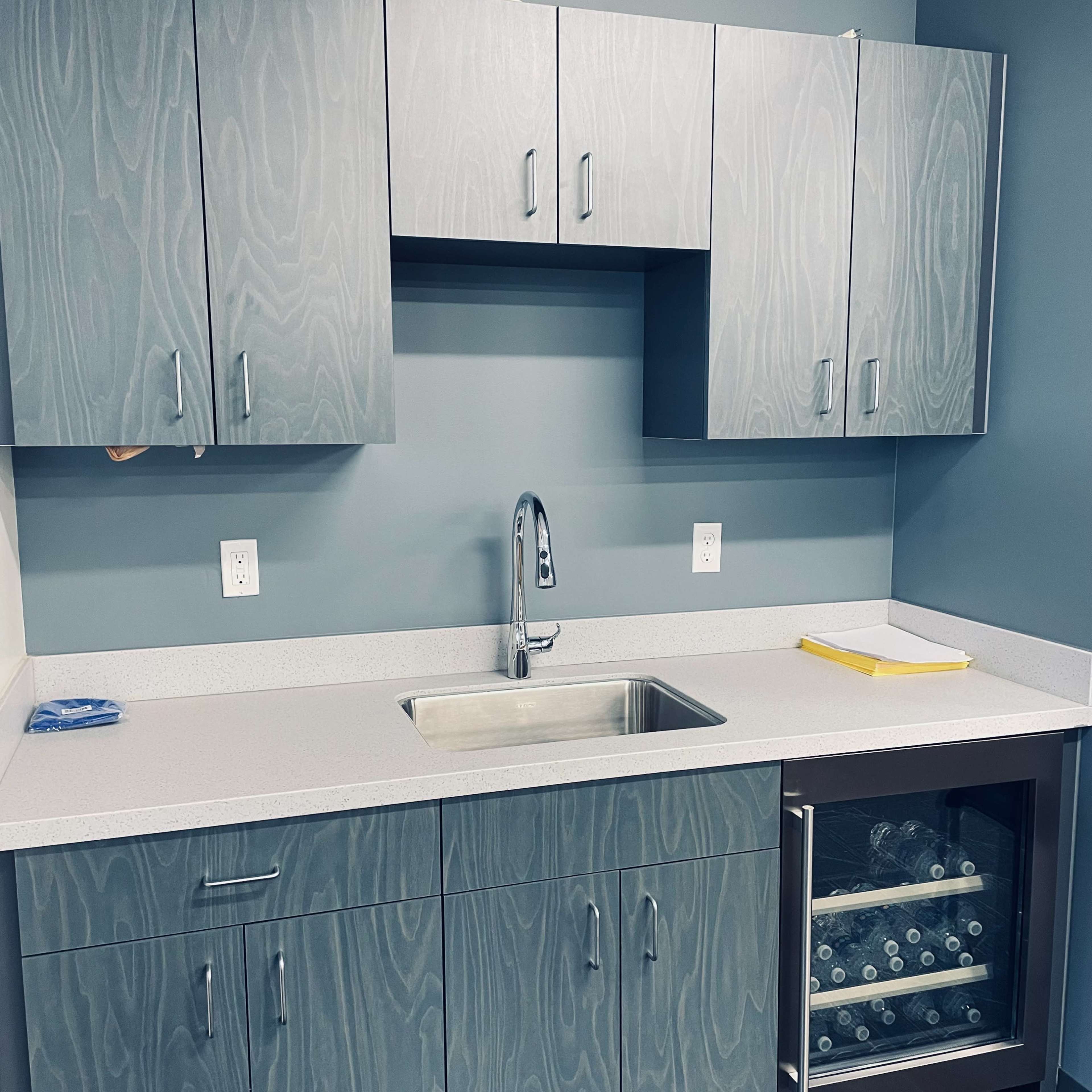 A modern kitchen area with gray cabinetry, a sink, and a small refrigerator below.