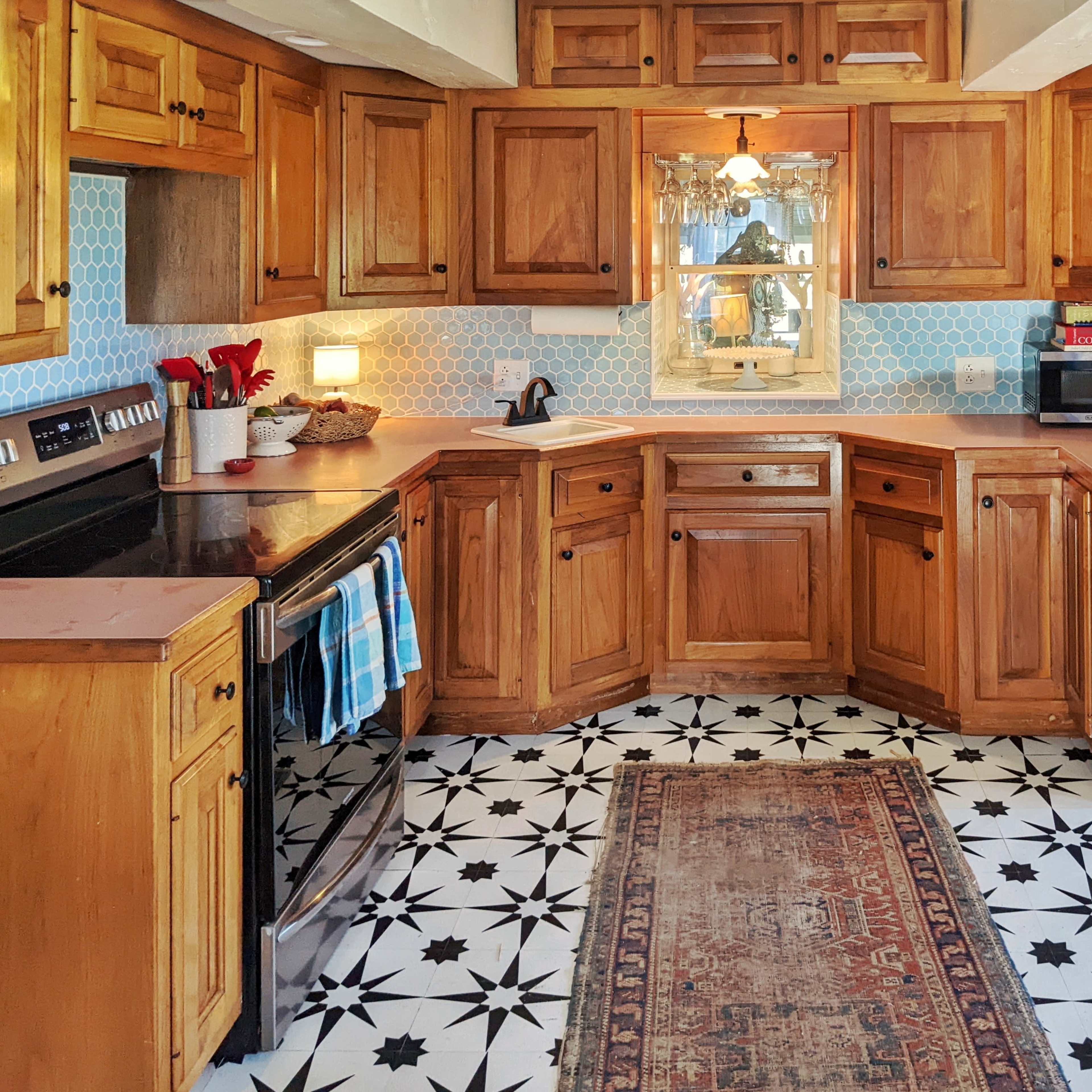 A kitchen with wooden cabinets, a patterned tile floor, and a central rug.