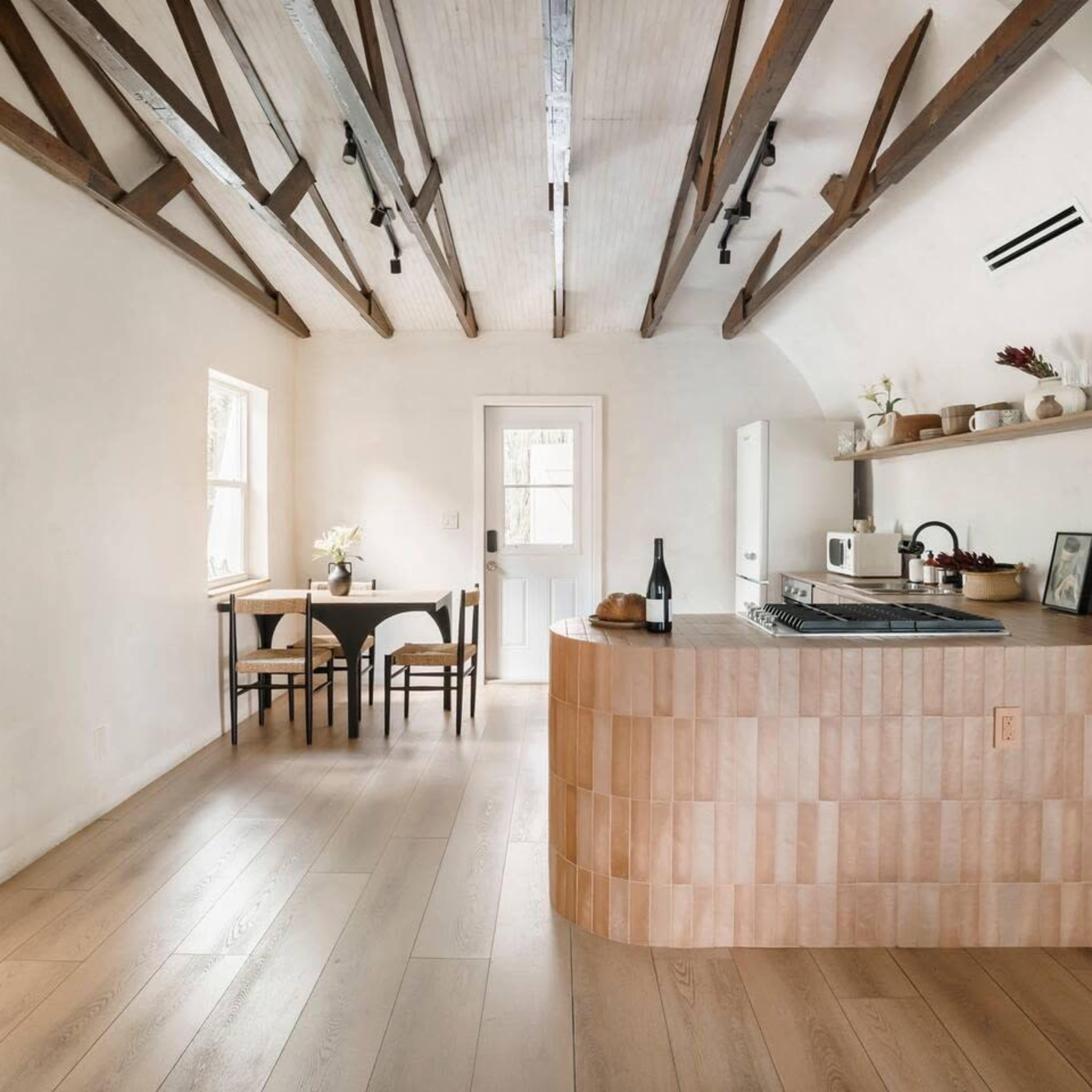 A modern kitchen and dining area with exposed wooden beams, a curved entryway, and a light-colored, minimalist design.
