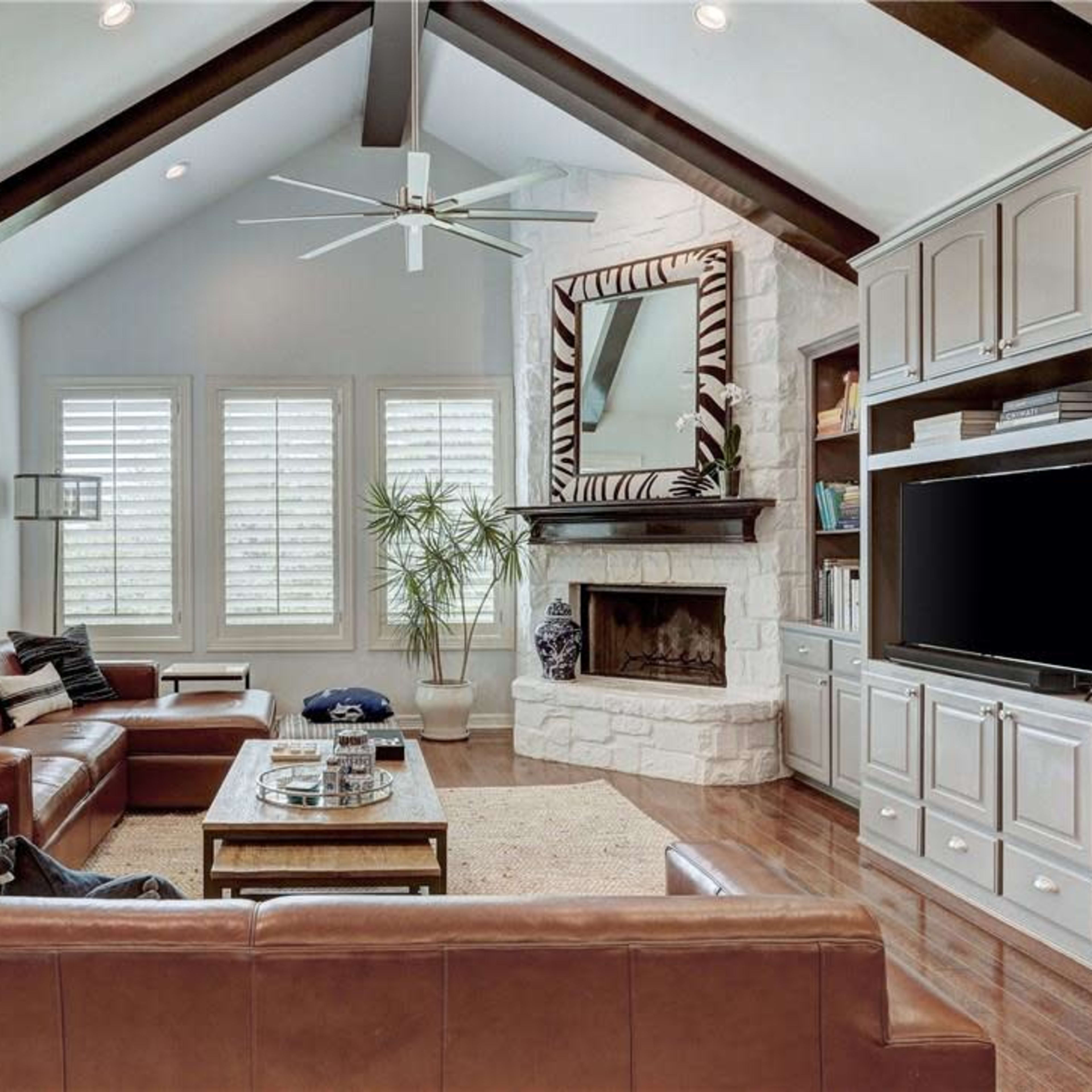 The living room features a high ceiling with exposed beams, a large fireplace, and contemporary furniture arranged around a central coffee table.