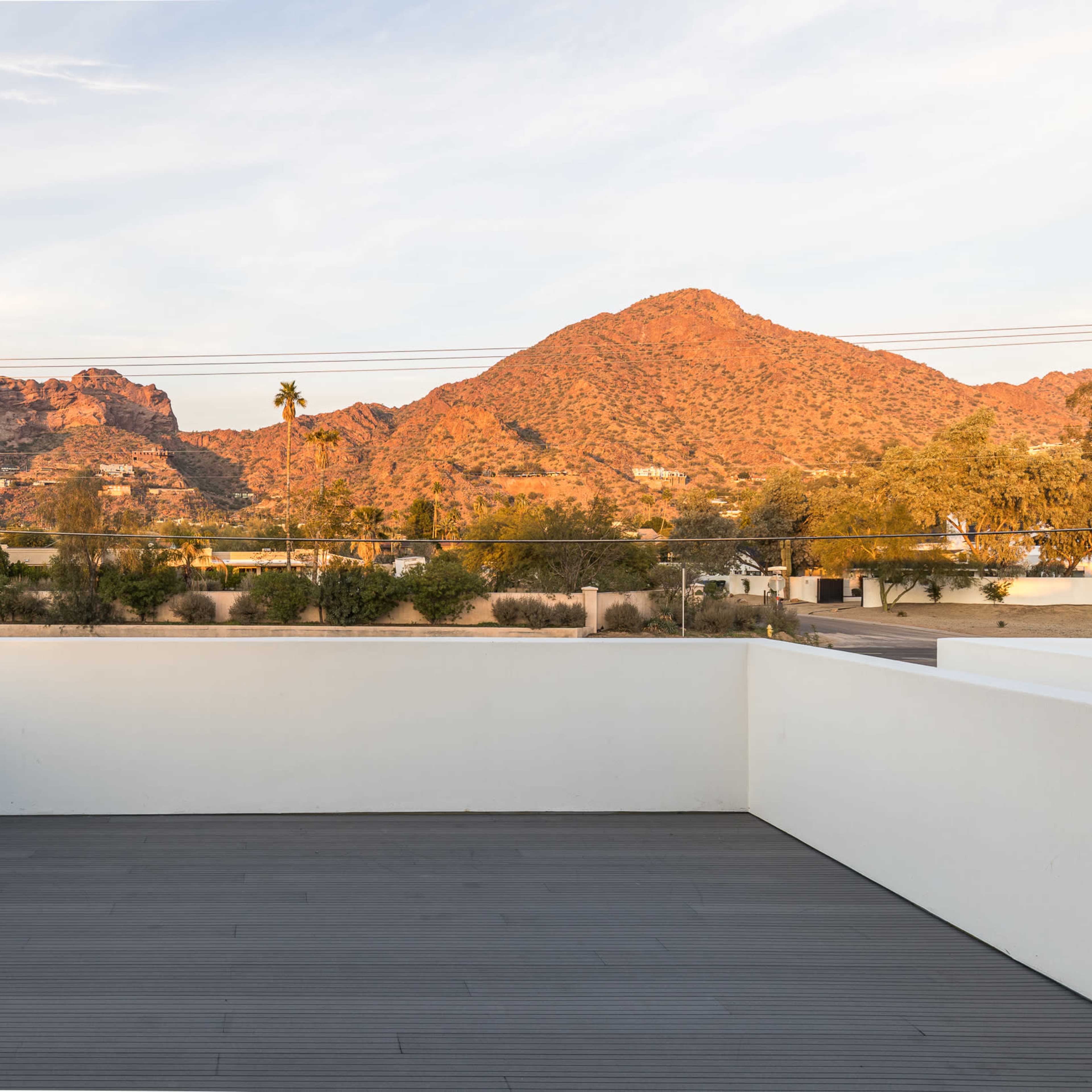 A spacious terrace with a wooden deck overlooking a mountainous landscape bathed in warm sunlight.