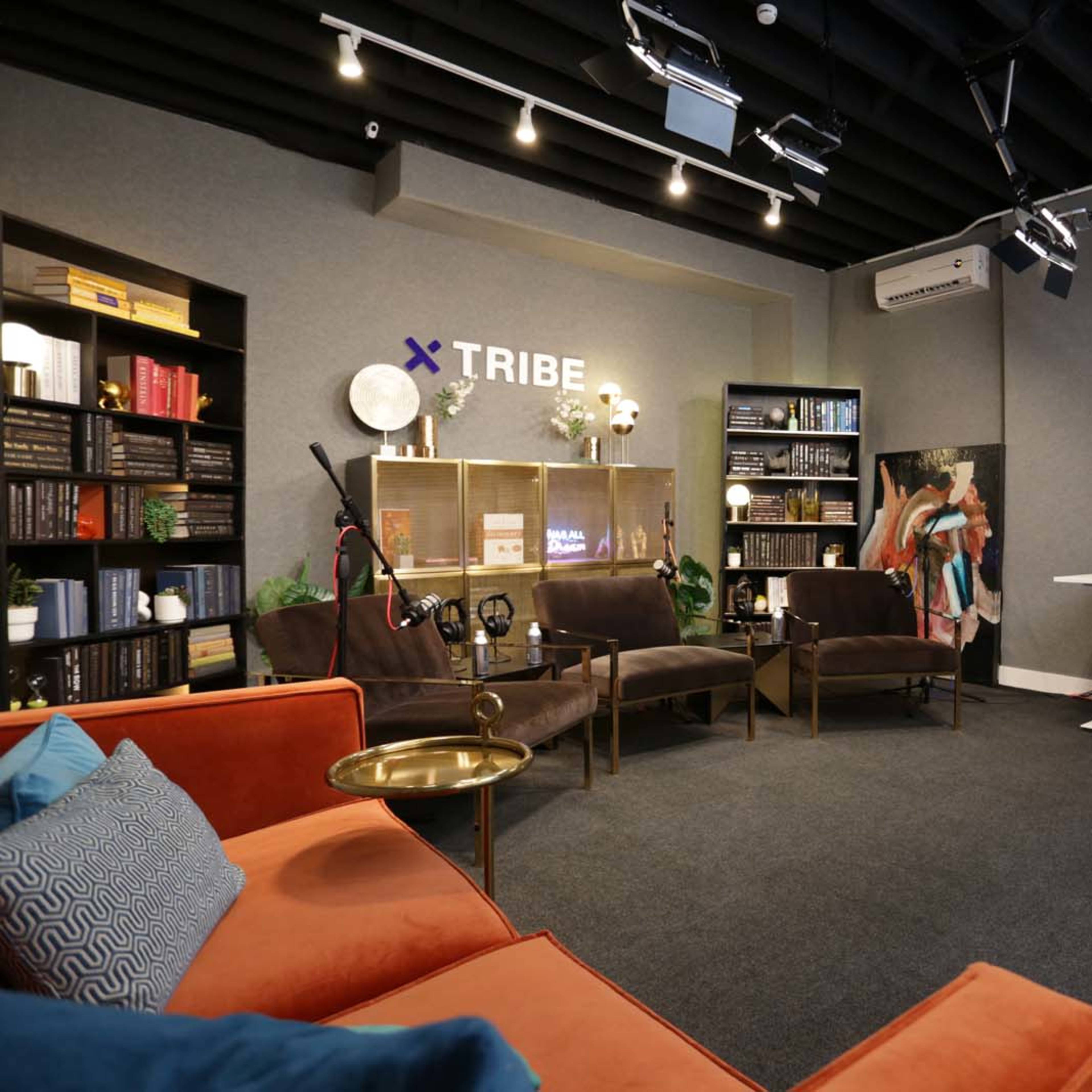 A modern studio setting with comfortable seating, bookshelves, and video equipment arranged for a podcast or interview.