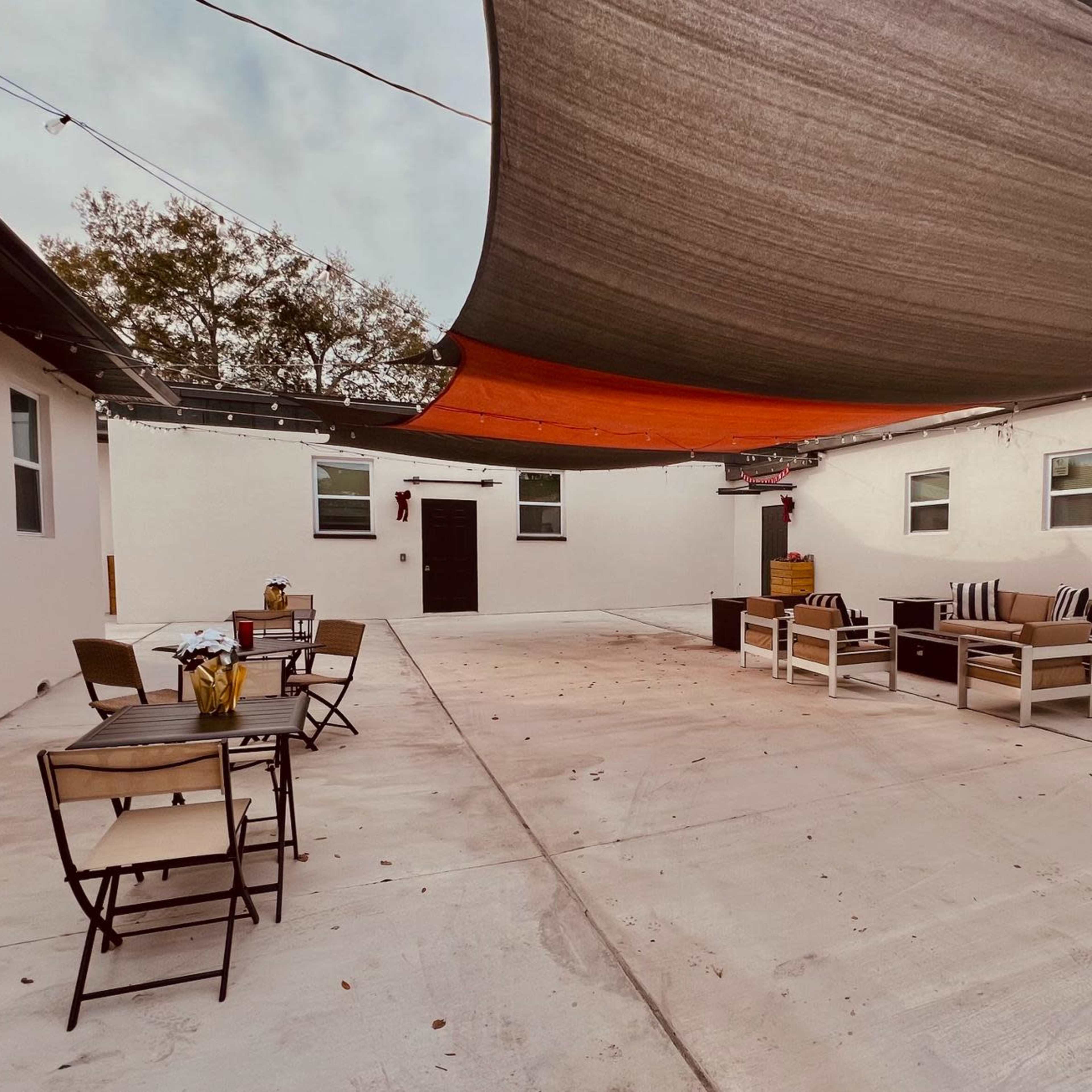 A spacious outdoor area with shaded seating arrangements, tables, and a concrete floor.