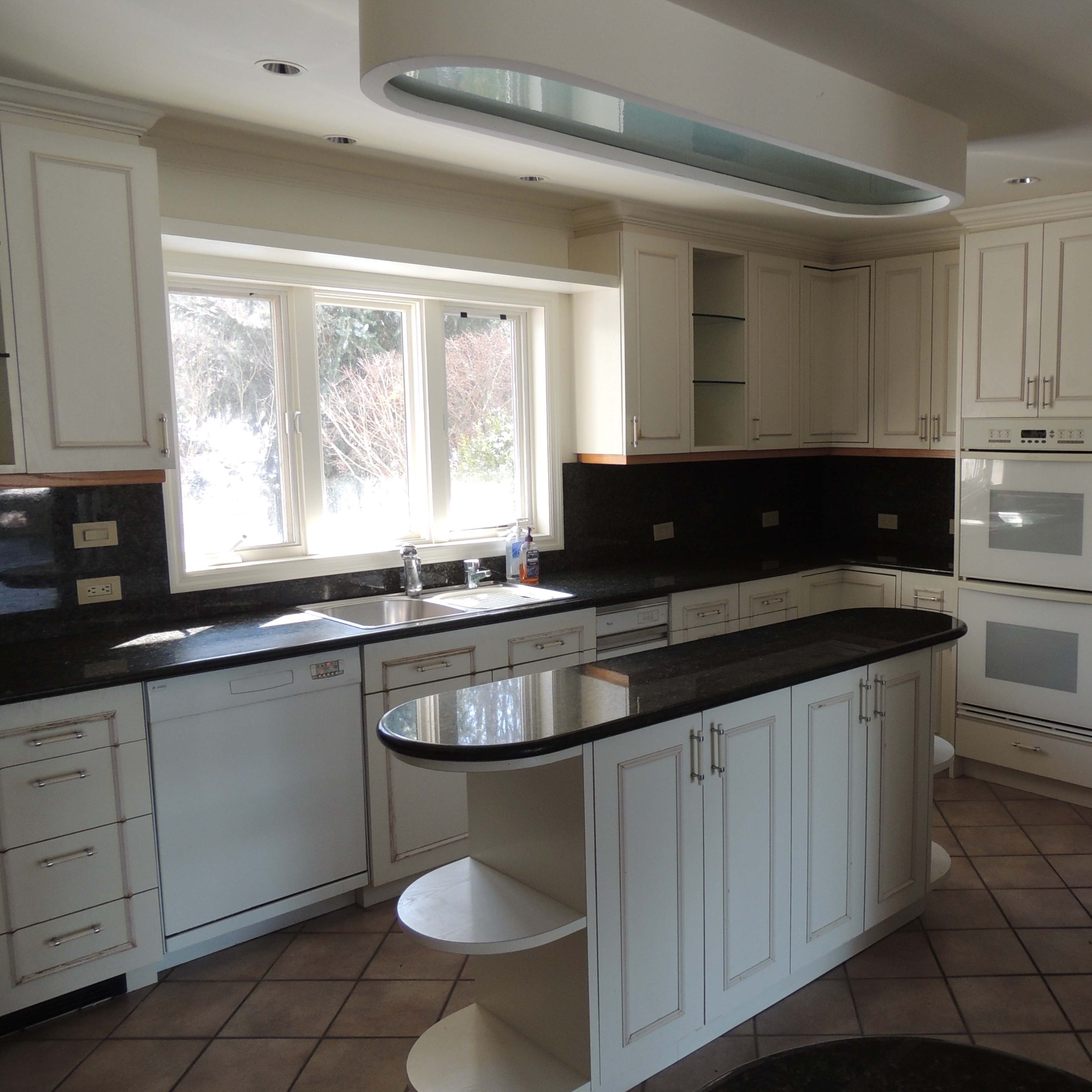 A modern kitchen with white cabinets, black countertops, and a large window providing natural light.
