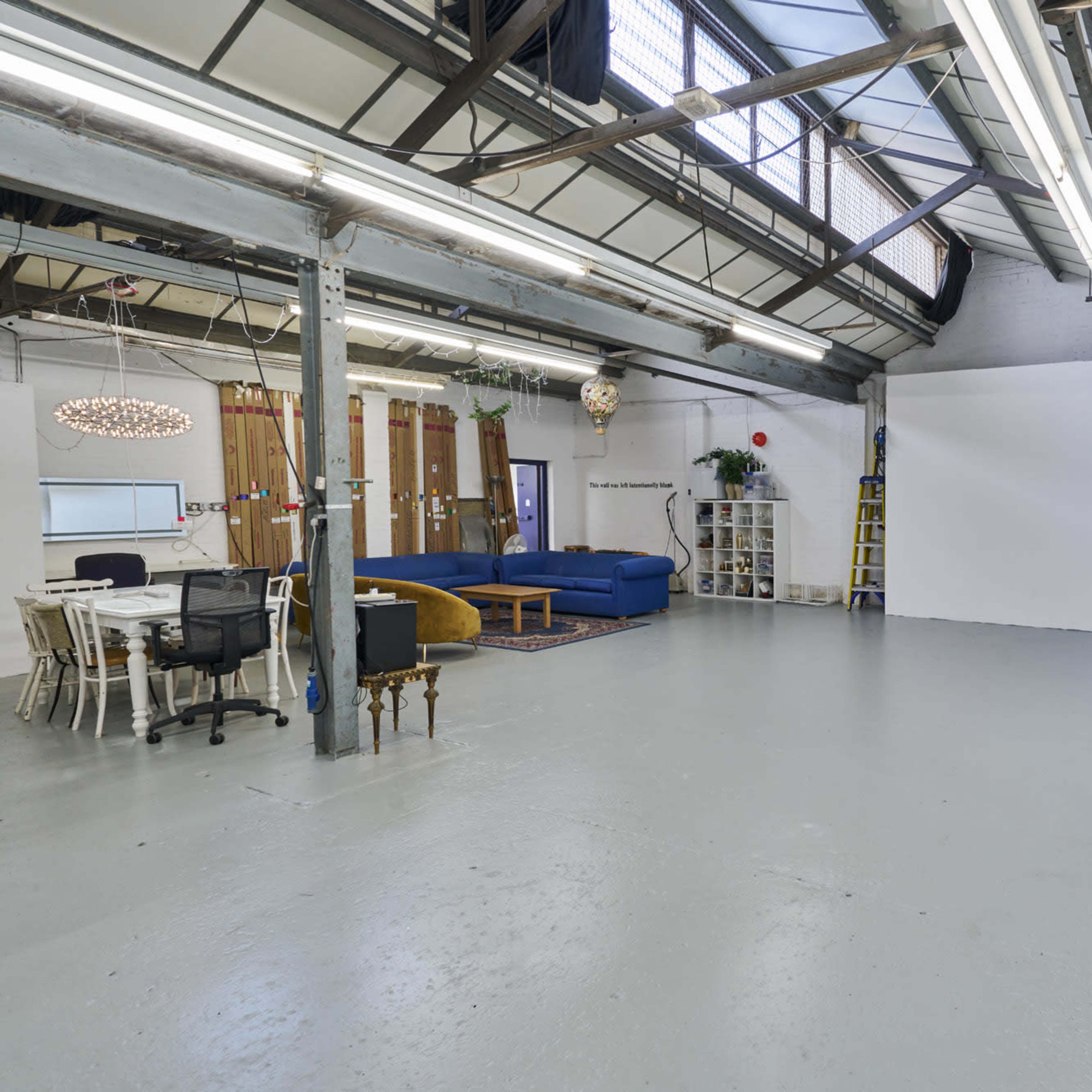 A spacious, industrial-style studio with a white wall, seating areas, and various workstations.