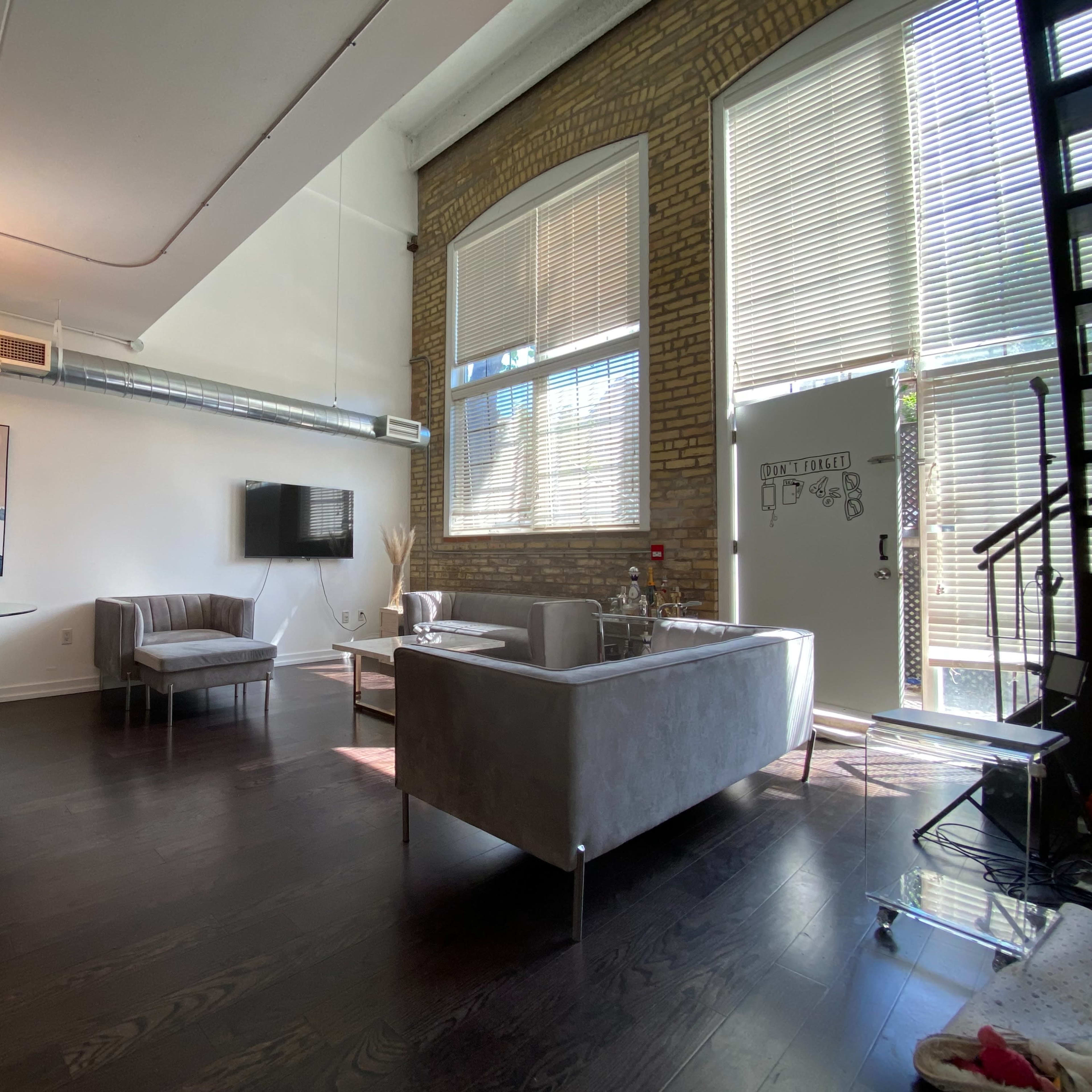 A modern interior space with a seating area, a dining table, and large windows that allow natural light to illuminate the room.