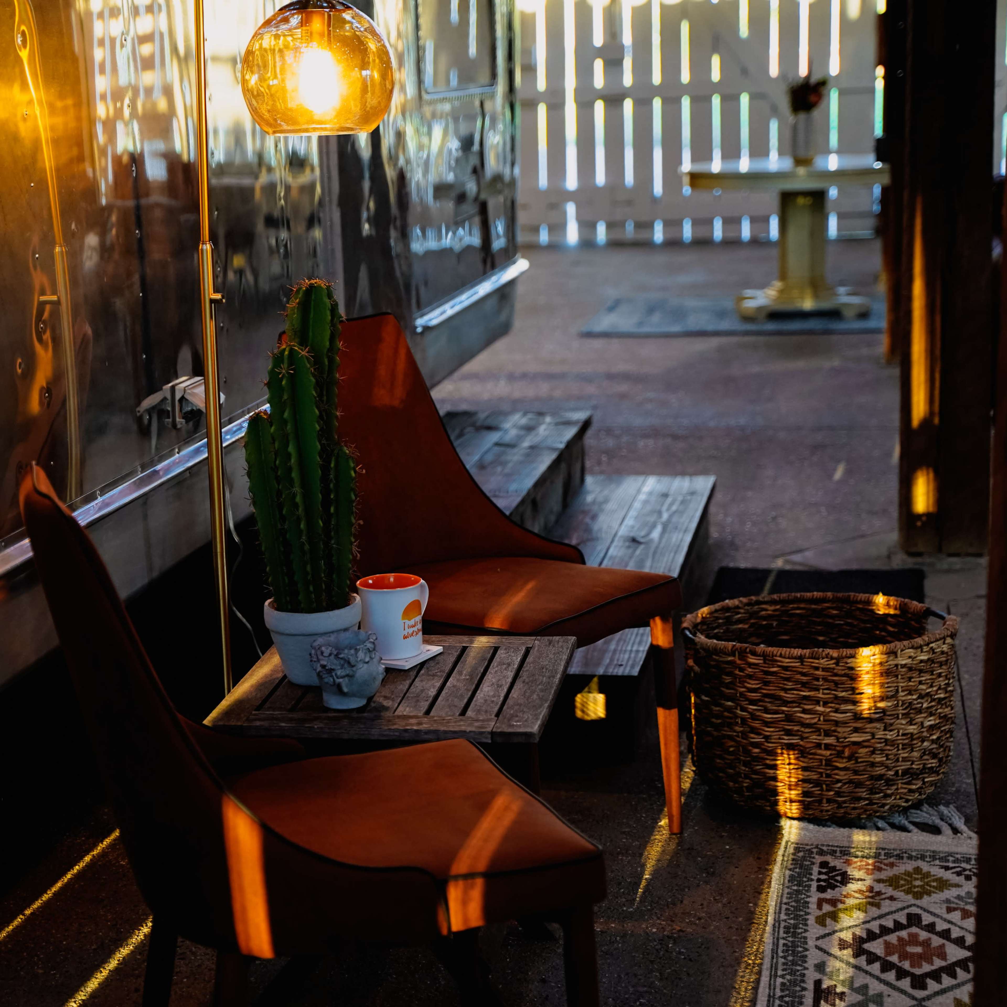 Two brown chairs are positioned next to a small table with a potted cactus and a cup, illuminated by pendant lights in an outdoor setting.