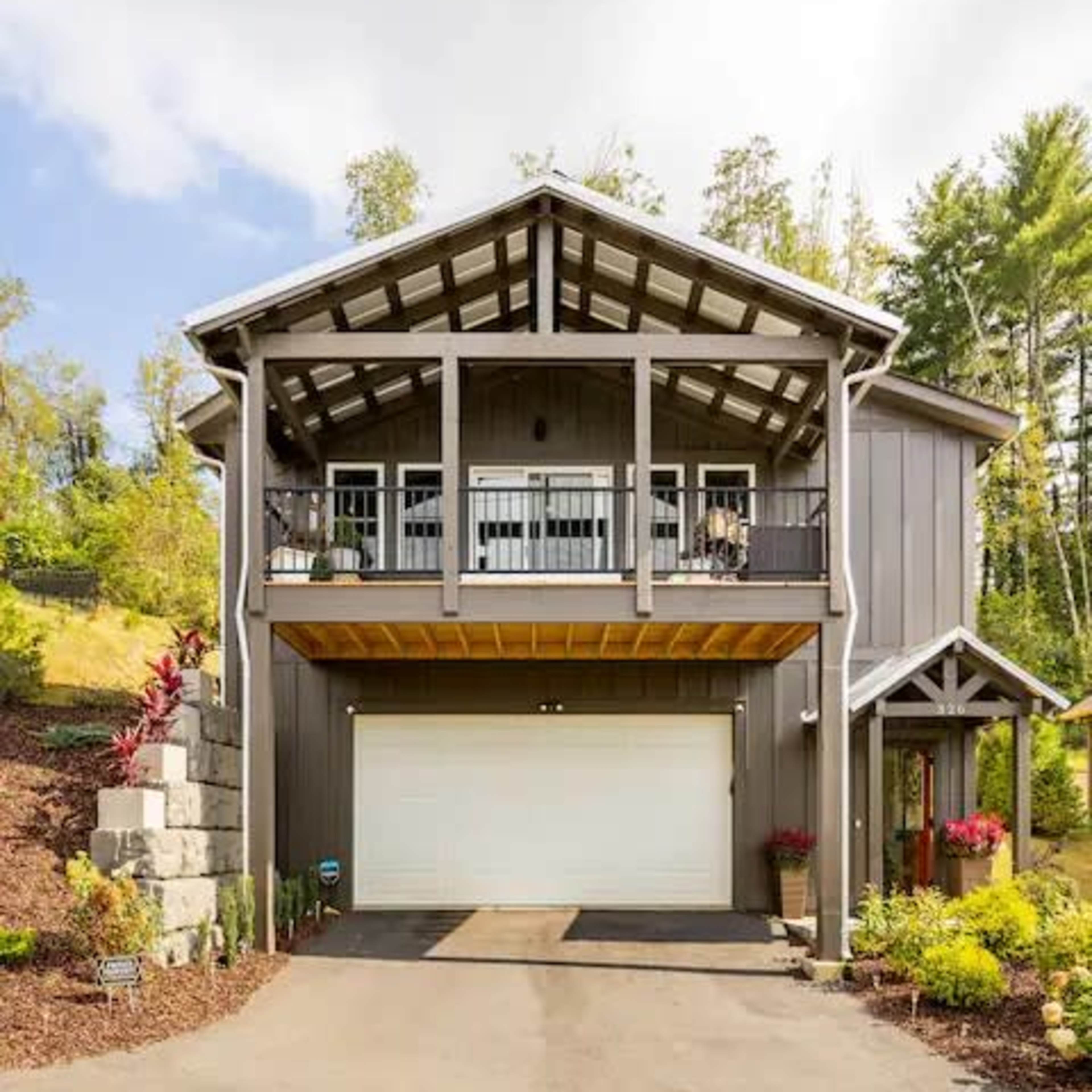 A two-story gray house with a front porch, balcony, and a garage is set on a landscaped lot.