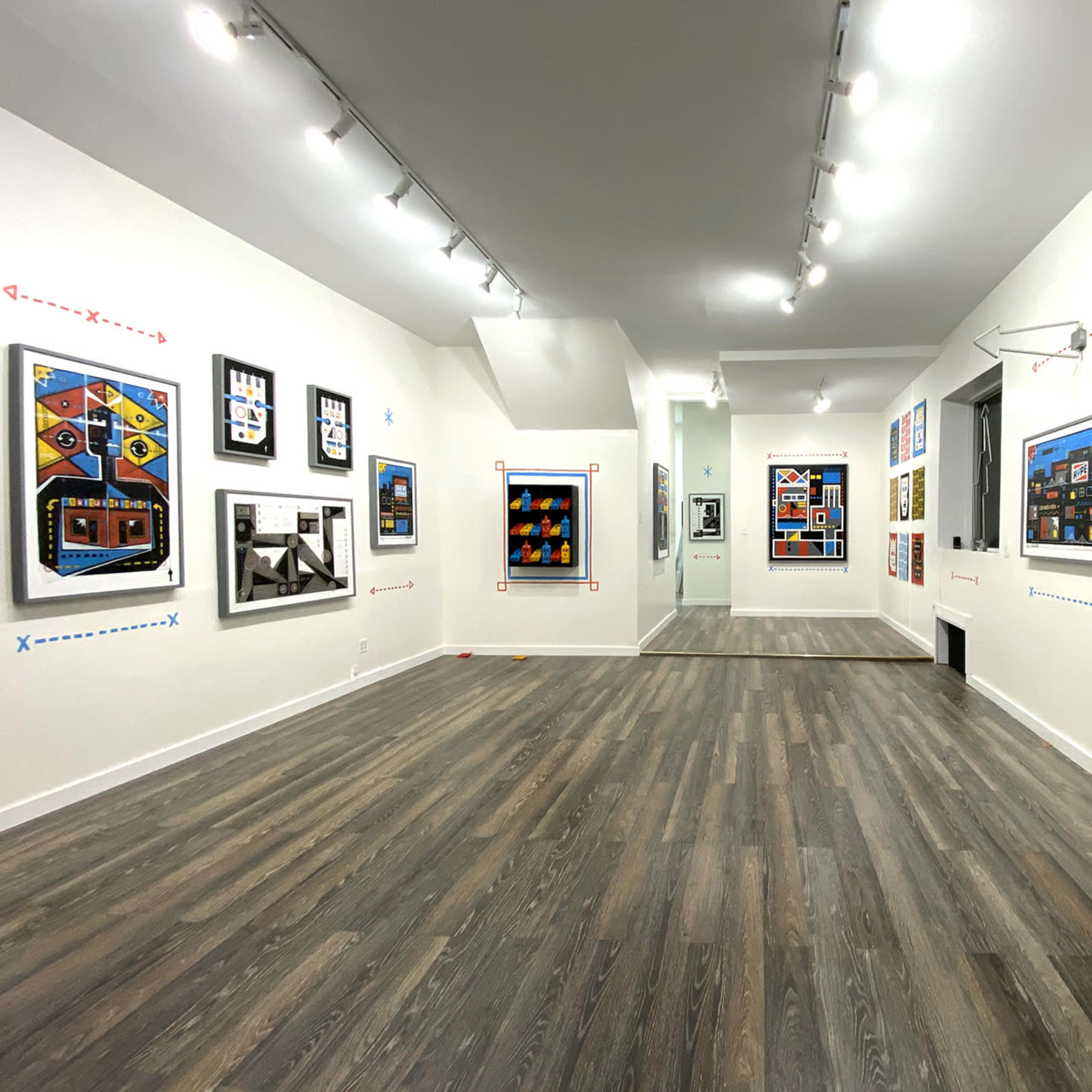 An art gallery with several colorful framed artworks displayed on white walls and a wooden floor.