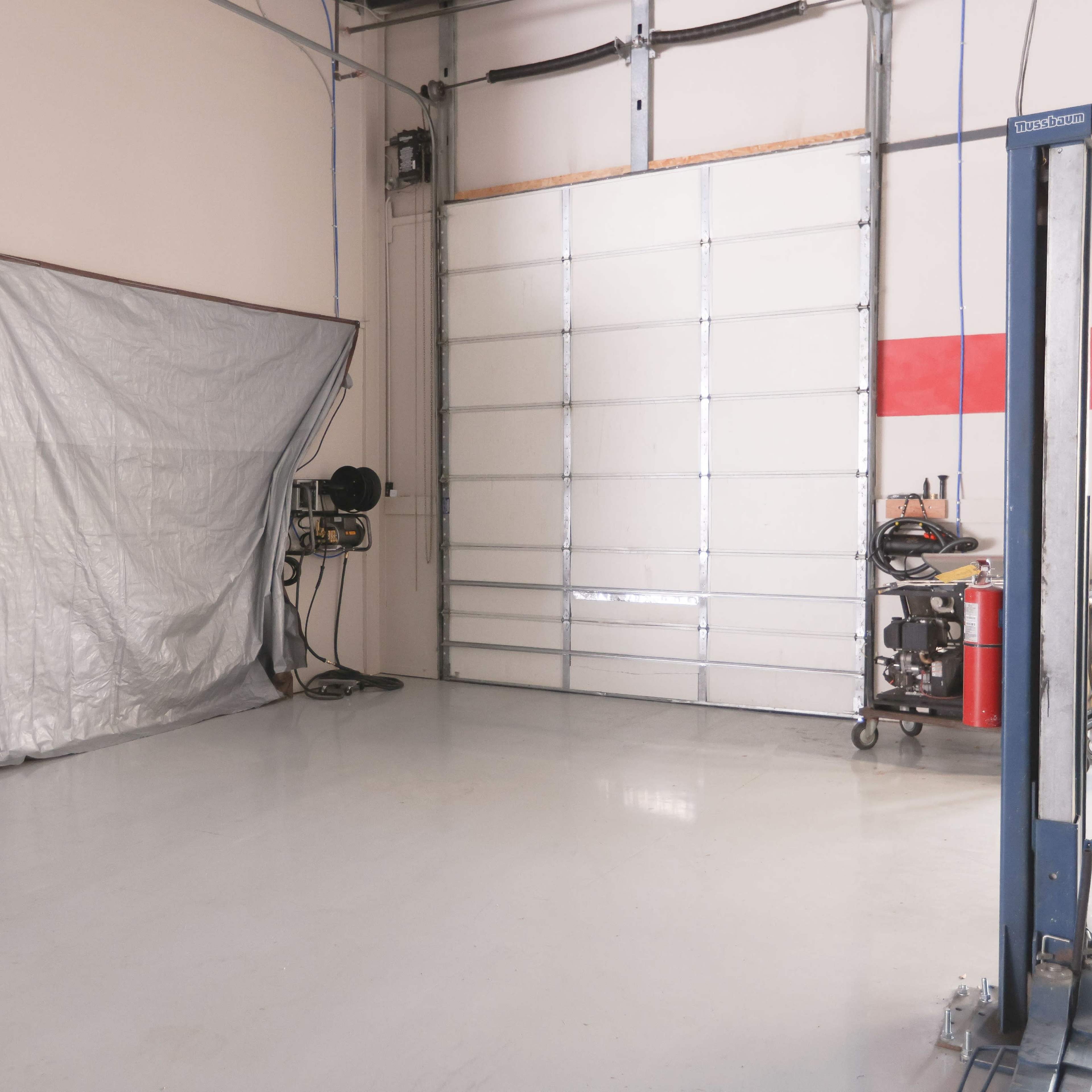 A spacious garage with a large roll-up door and a gray tarp partially covering an area on the left side.