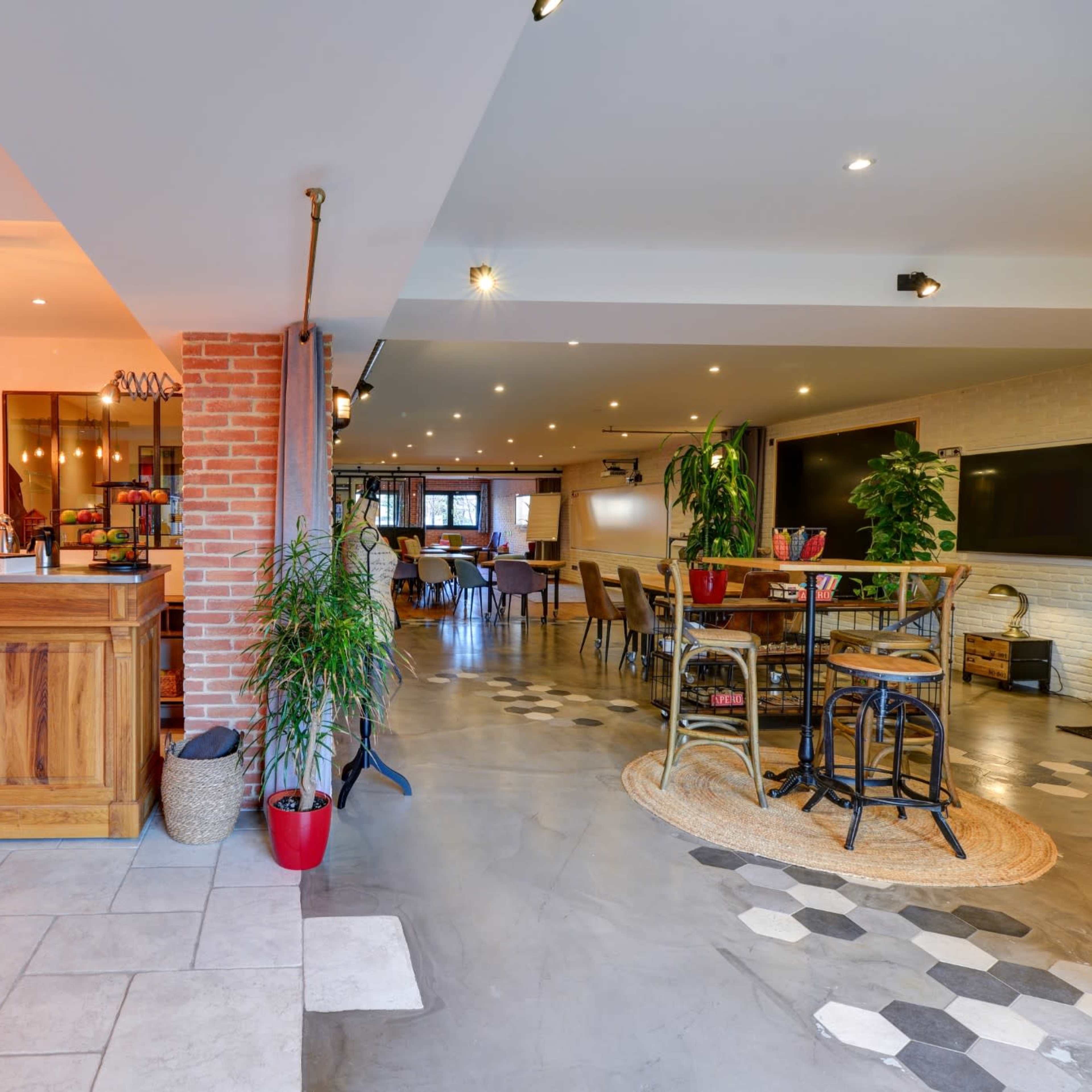 A modern interior space featuring a wooden bar area with a vibrant orange wall, leading into a dining area with varied seating arrangements and decorative plants.