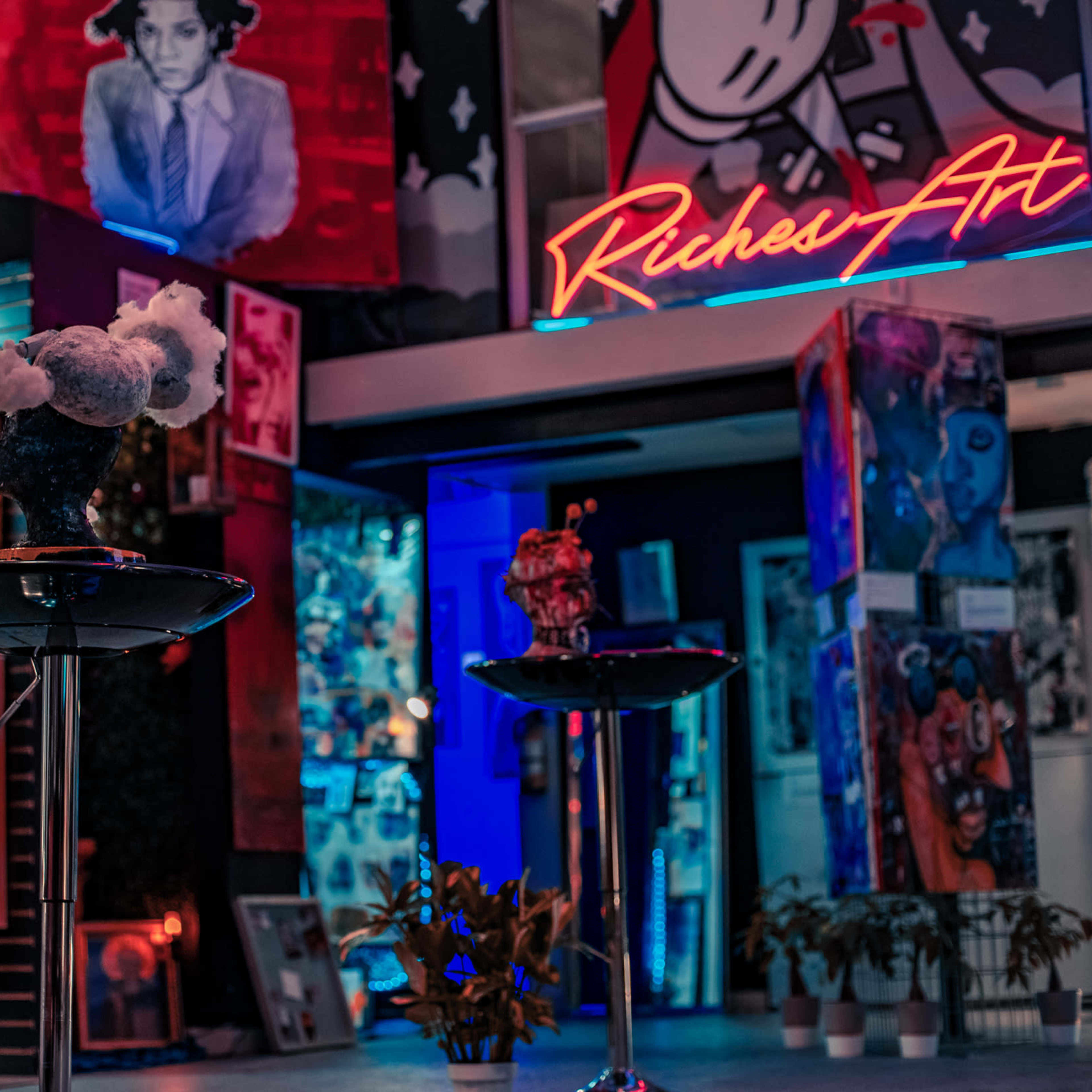 A vibrant art gallery featuring colorful murals and art pieces illuminated by neon signs and ambient lighting.