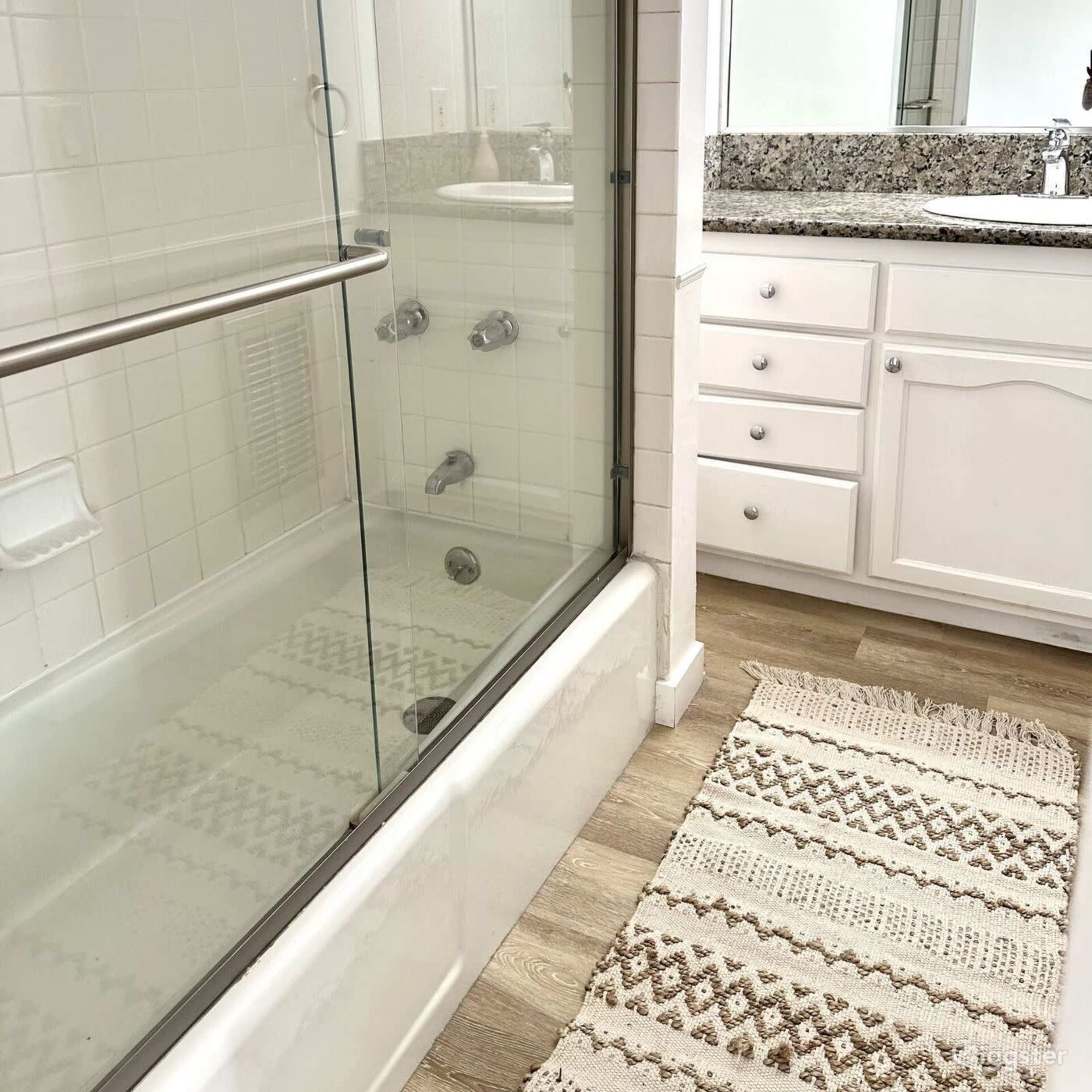 A bright bathroom features a glass shower enclosure beside a white vanity with a granite countertop and a mirror.