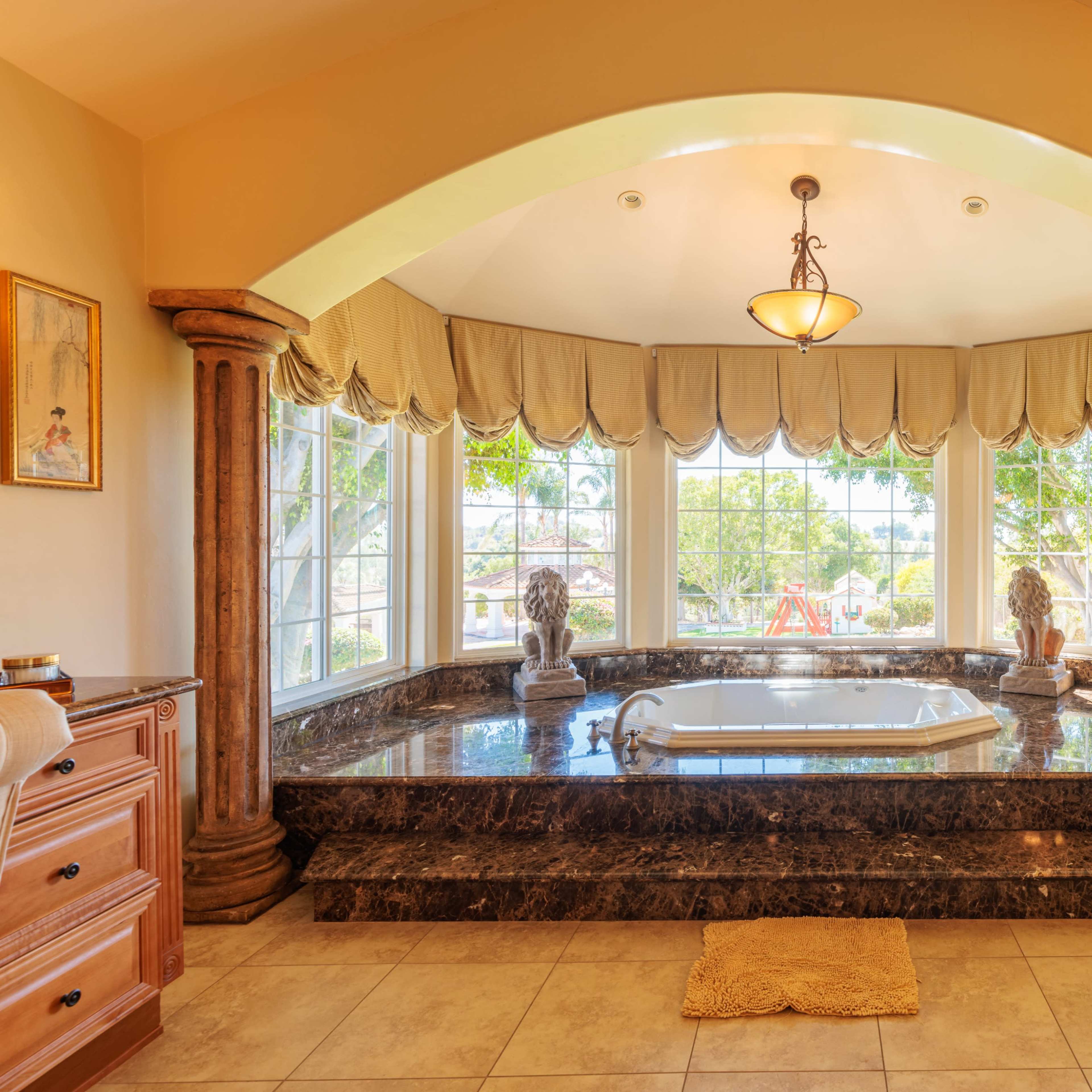 A spacious bathroom featuring a large jetted tub surrounded by a marble platform, with multiple windows providing outdoor views.