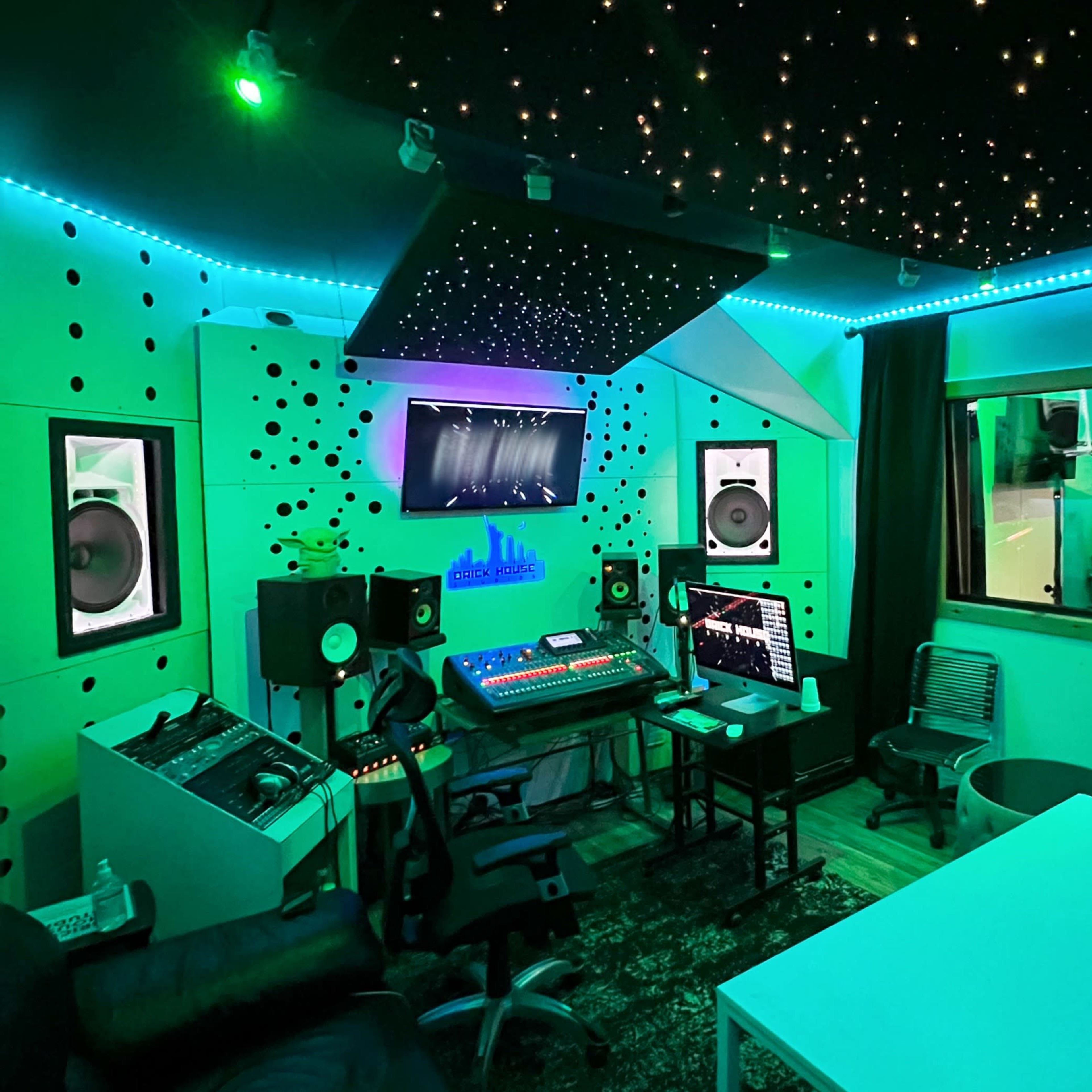 A modern recording studio with colorful LED lighting, sound equipment, and a vocal booth visible through a window.