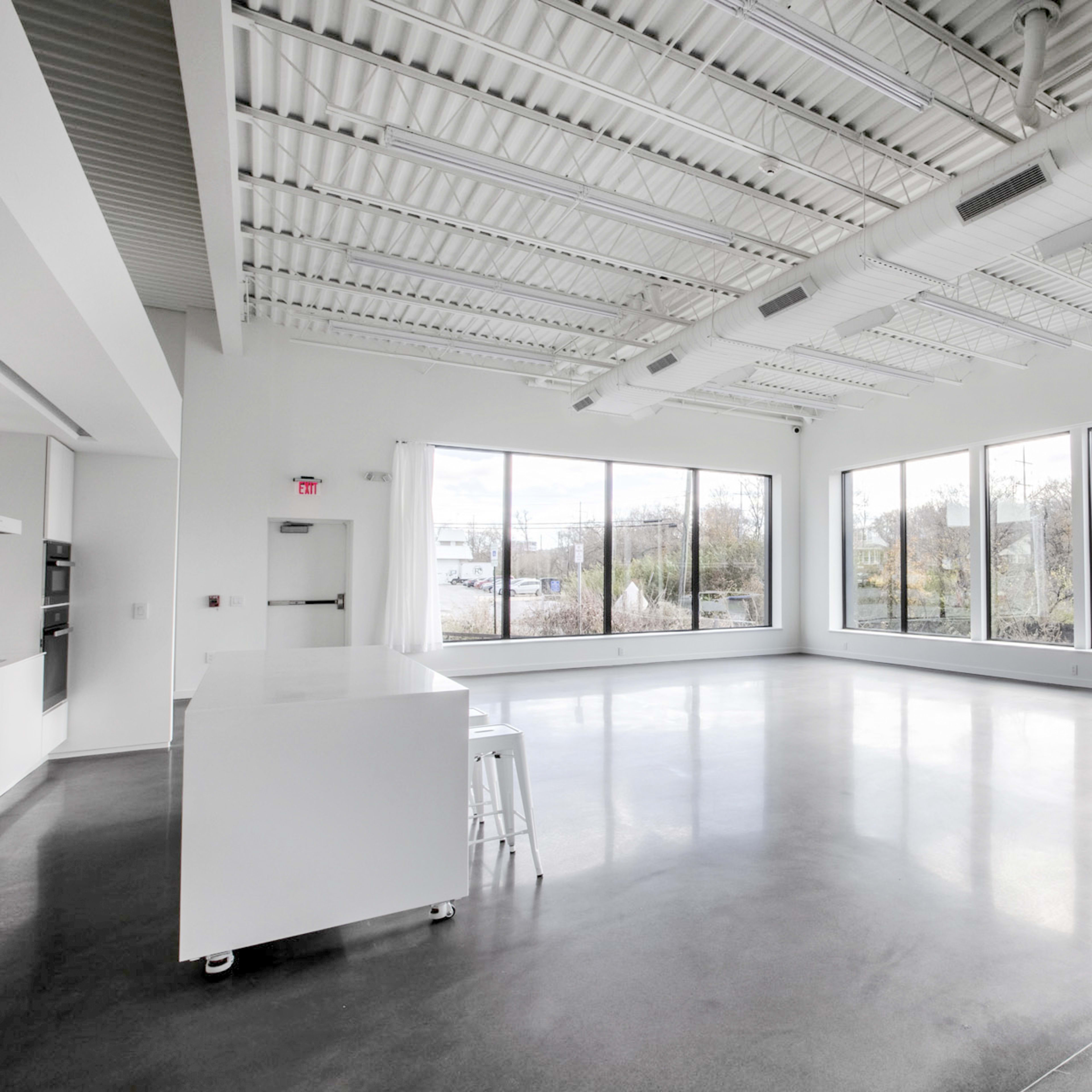 A spacious, empty room with large windows and a kitchen area featuring a white countertop.