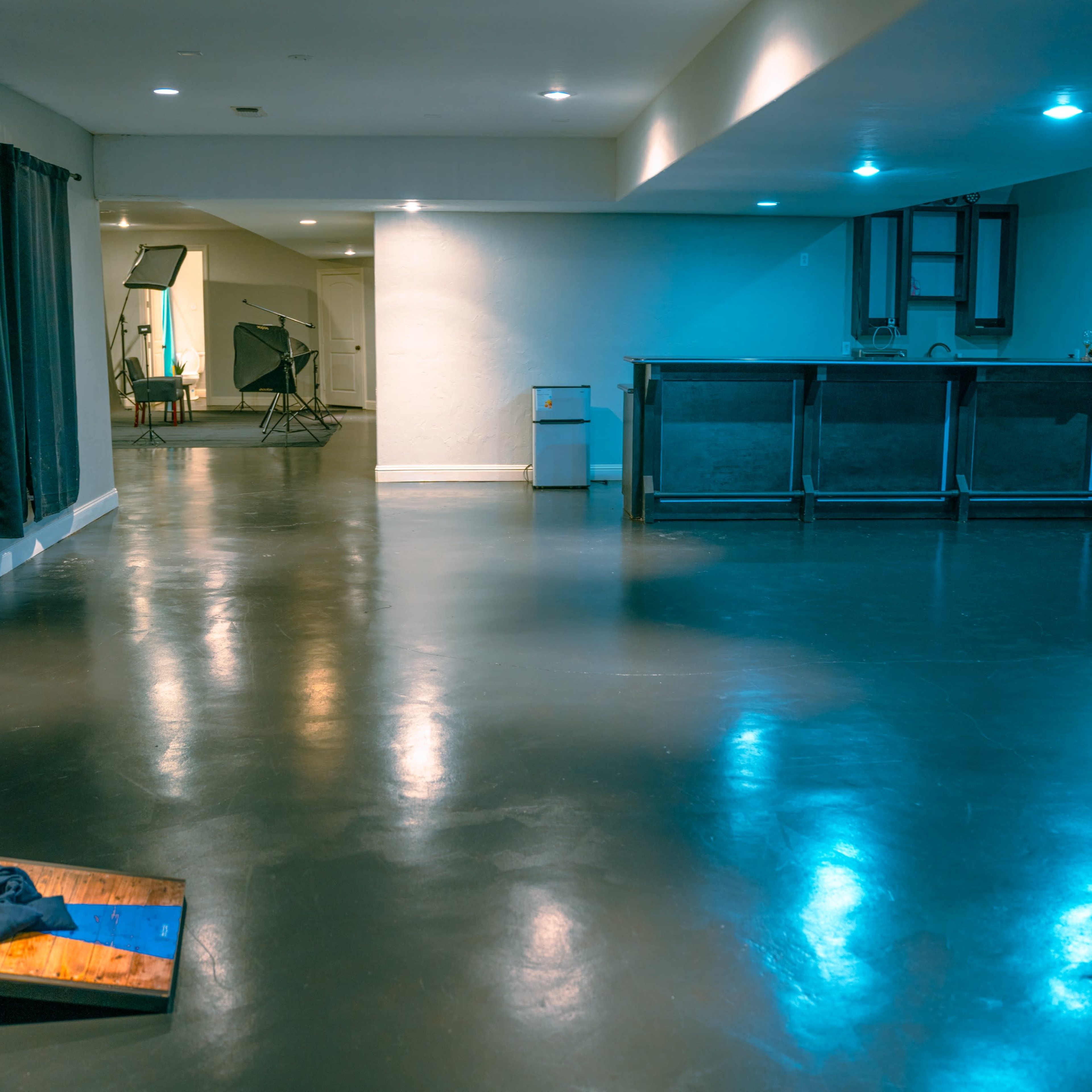 A spacious room with polished dark floors, a bar area in the back, and a cornhole game on the left.