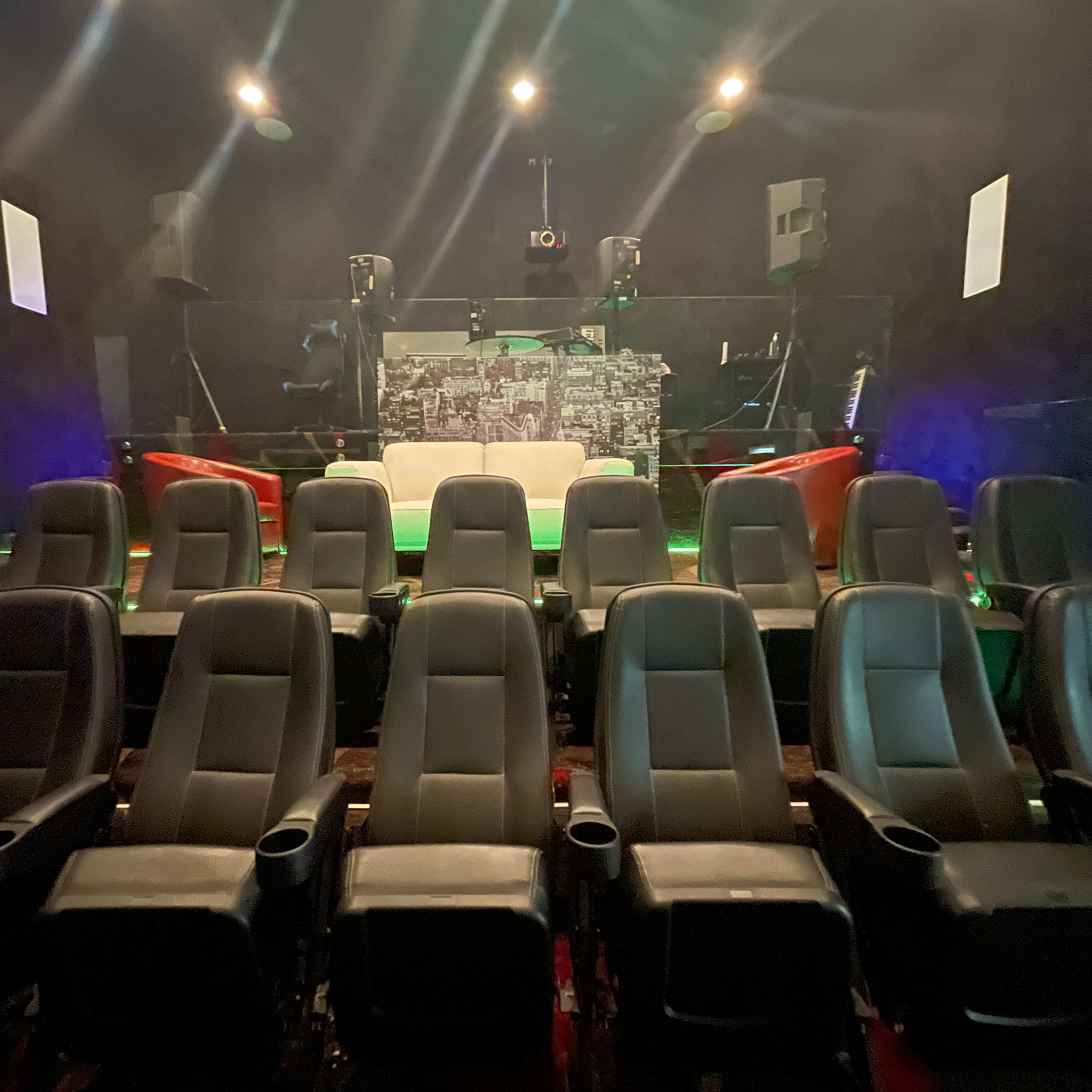 A row of black cinema chairs facing a blank screen in a dimly lit theater.